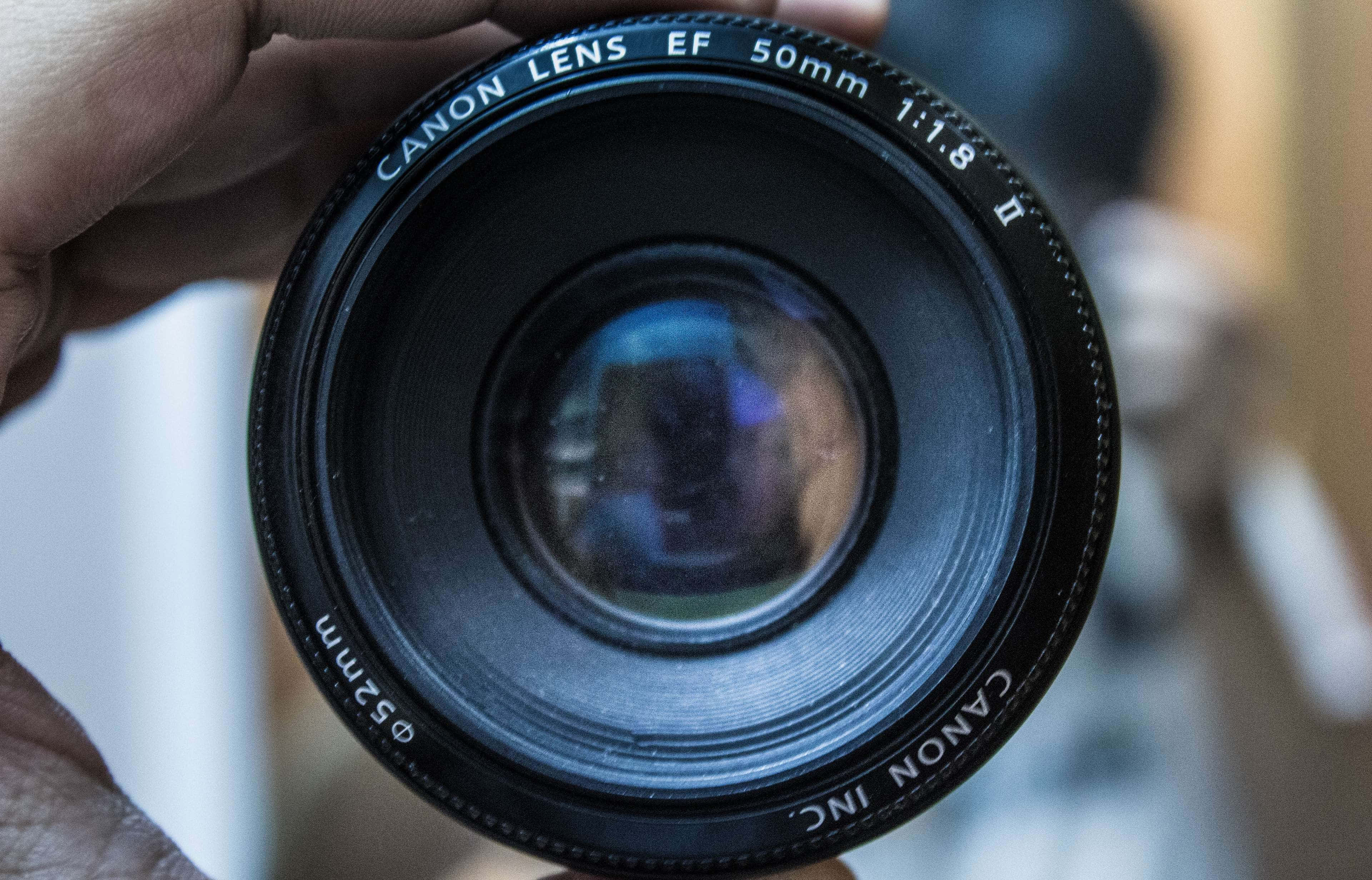 Cameraman 桌布 壁紙 — 手持黑色Canon EF 50mm f/1.8鏡頭的近距離特寫，背景反射模糊。