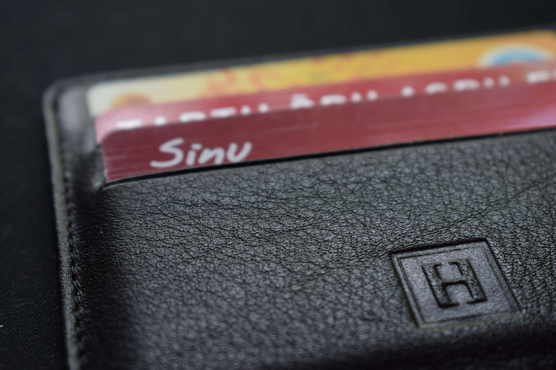  壁紙 — 黑色皮革錢包特寫，一張標有「Sinu」的卡片在深色背景中露出。