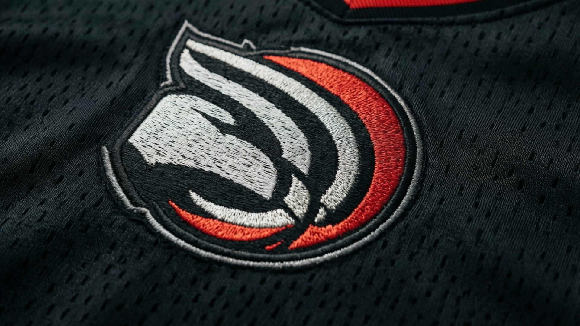 Jersey Logo Detail 壁紙 — 黑色網眼運動球衣的特寫，帶有白色、灰色和紅色刺繡的標誌。