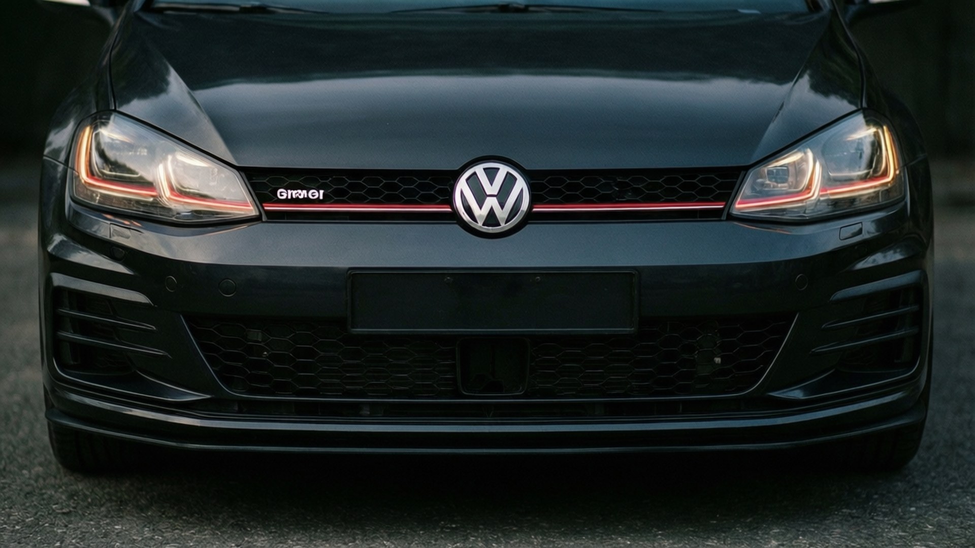 GTI Grille Detail 壁紙 — 黑色福斯 Golf GTI 前水箱護罩特寫，帶有紅色飾條和發光頭燈。