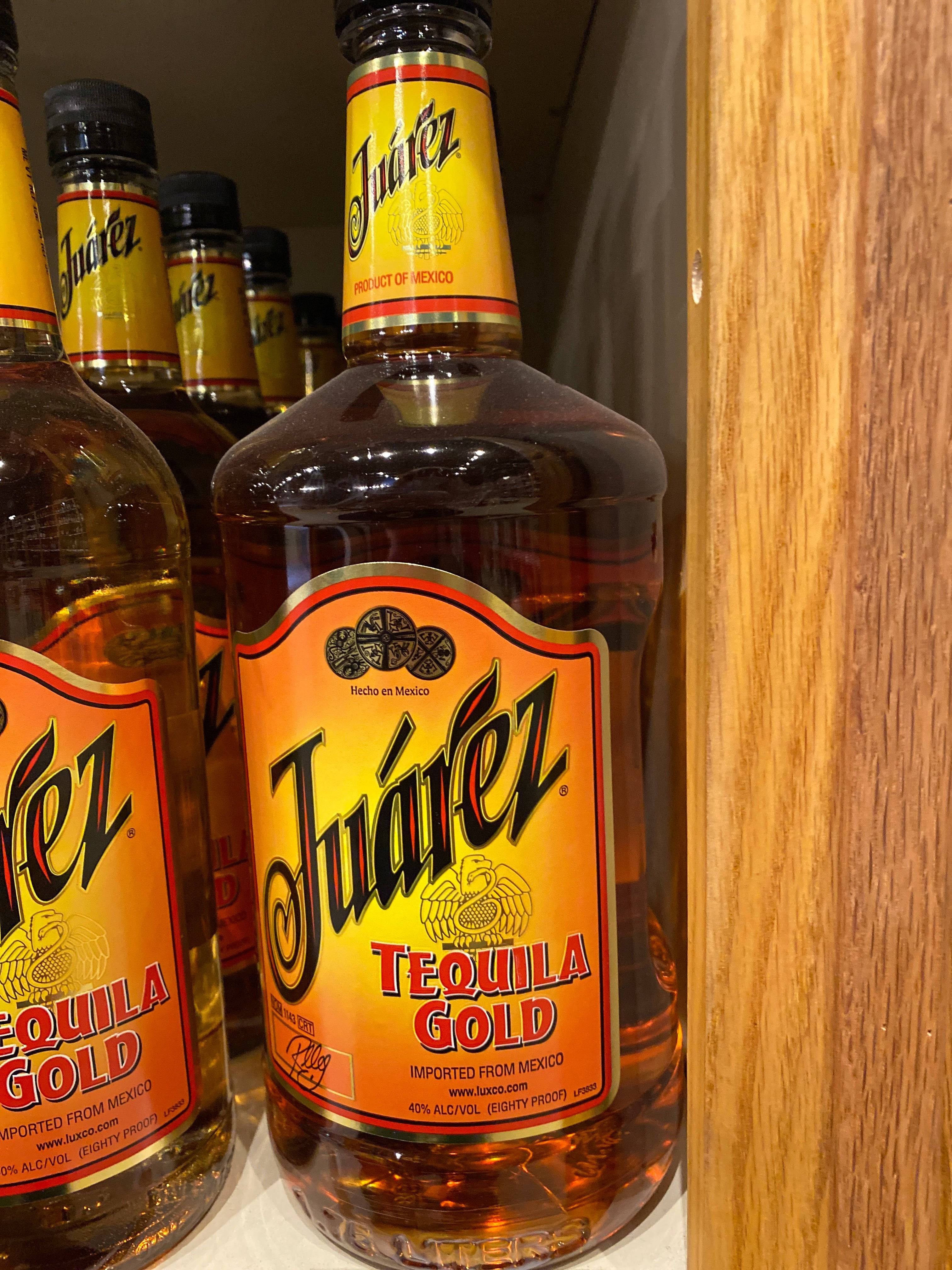 bottle 桌布 壁紙 — Juárez Tequila Gold 酒瓶的特寫，放在木架上，背景有其他酒瓶。