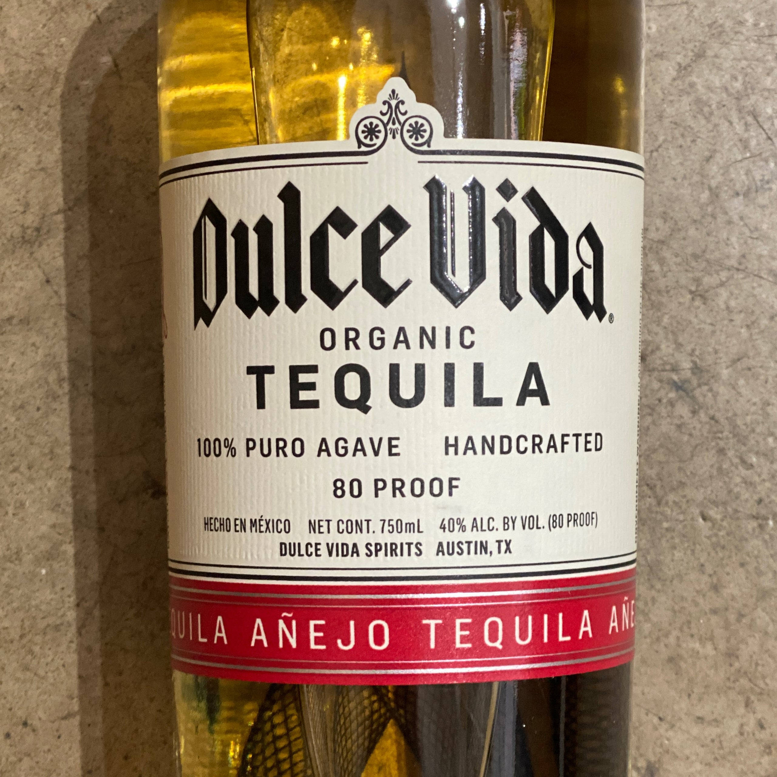 cocktail 桌布 壁紙 — Dulce Vida Organic Tequila 酒瓶標籤的特寫，顯示粗體字體和紅色條紋，背景為紋理石面。