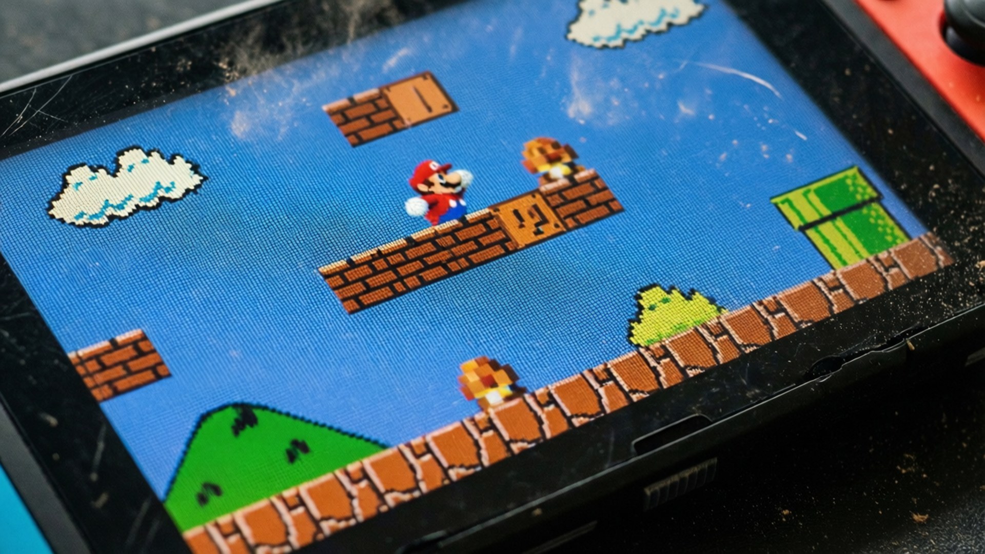 Macro Switch Screen 壁紙 — 一個佈滿灰塵的手提遊戲機螢幕特寫，顯示一個像素化的瑪利歐遊戲，有雲朵、磚塊和綠色管道。