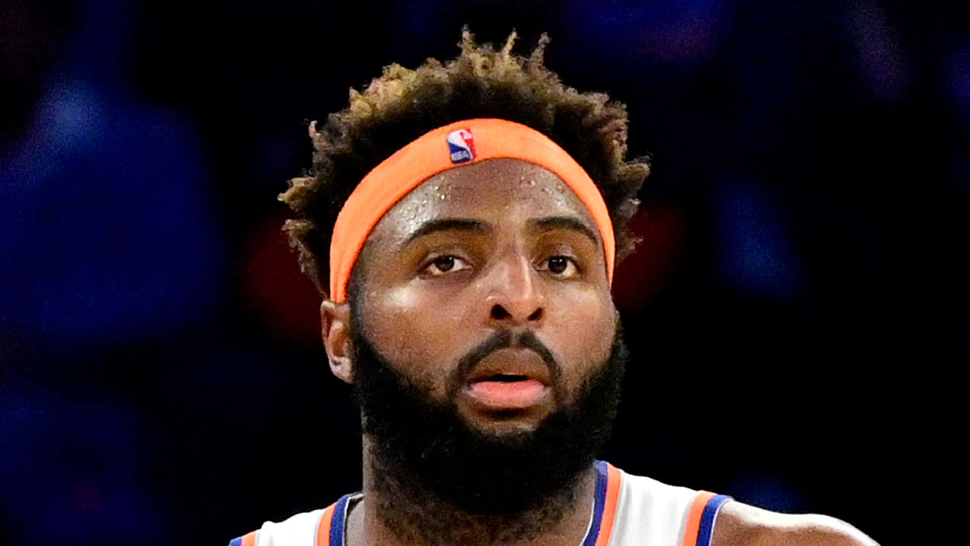 留鬍鬚、戴橙色頭帶的籃球運動員在比賽中專注。 — NBA 壁紙