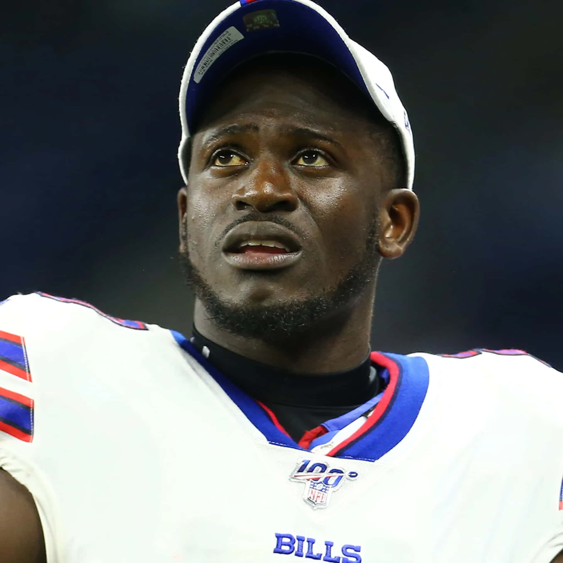  壁紙 — 專注的 Buffalo Bills 美式足球員身穿白色球衣和帽子，在球場燈光下的特寫。