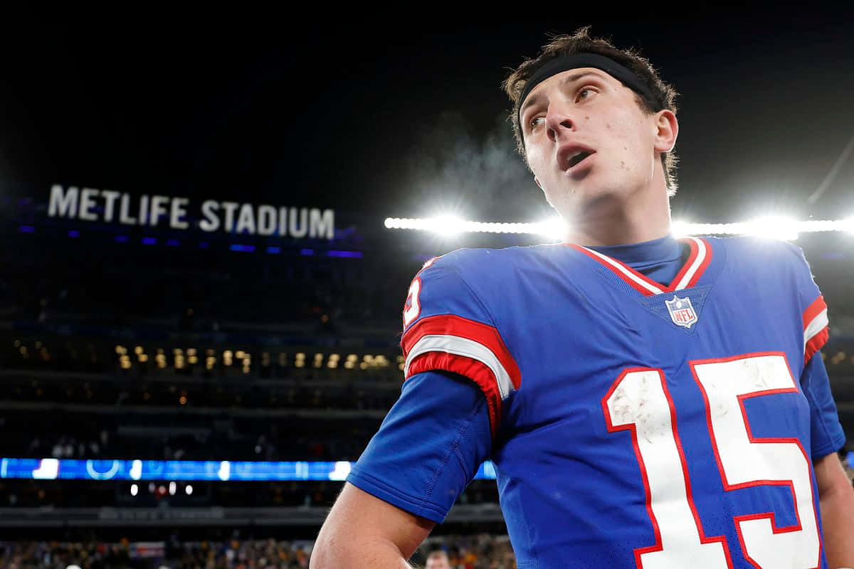  壁紙 — 一名身穿藍色15號球衣的足球員在MetLife Stadium的球場燈光下向上看的特寫。