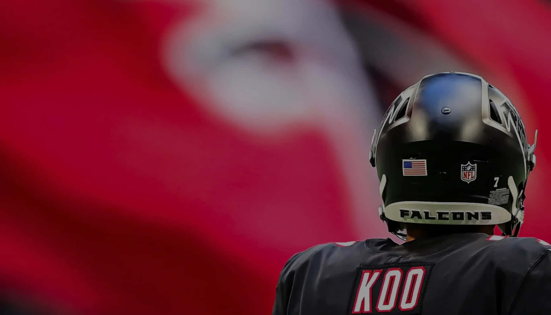  壁紙 — 一名美式足球員的近距離特寫，身穿黑色 Falcons 頭盔和球衣，背面印有 'KOO'，站在模糊的紅旗前。