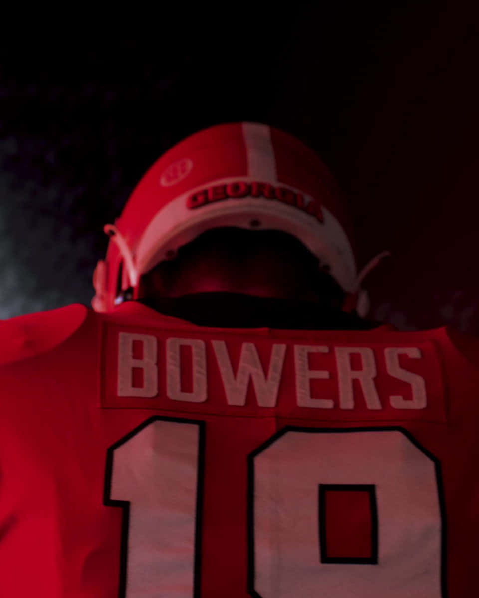  壁紙 — 近距離拍攝一名足球員的紅色球衣，上面有「BOWERS」和10號，頭盔下昏暗的紅色燈光。