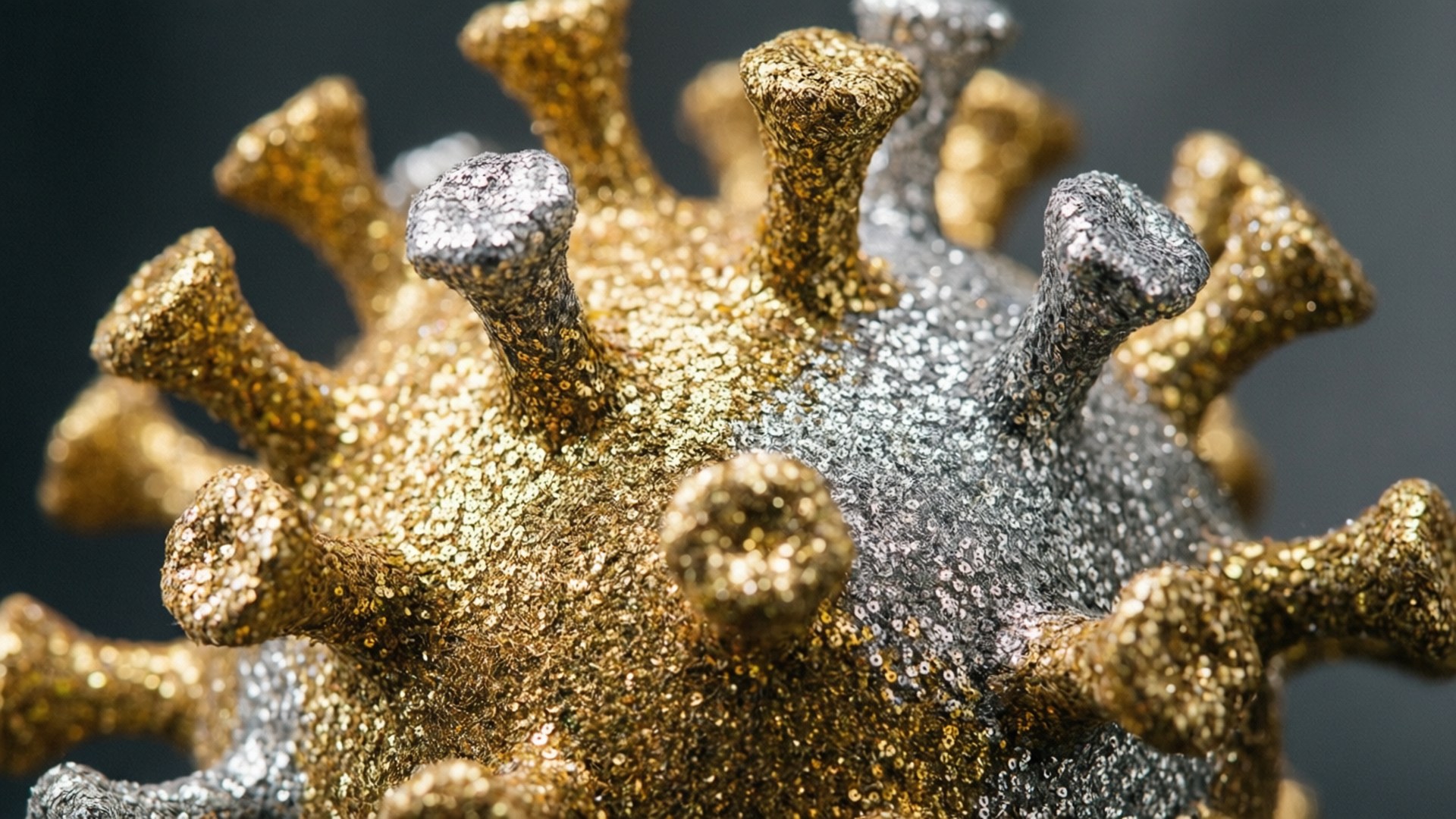 Glittering Gold Virus 壁紙 — 金色和銀色閃閃發光的冠狀病毒模型特寫，帶有紋理尖刺，背景為深色。