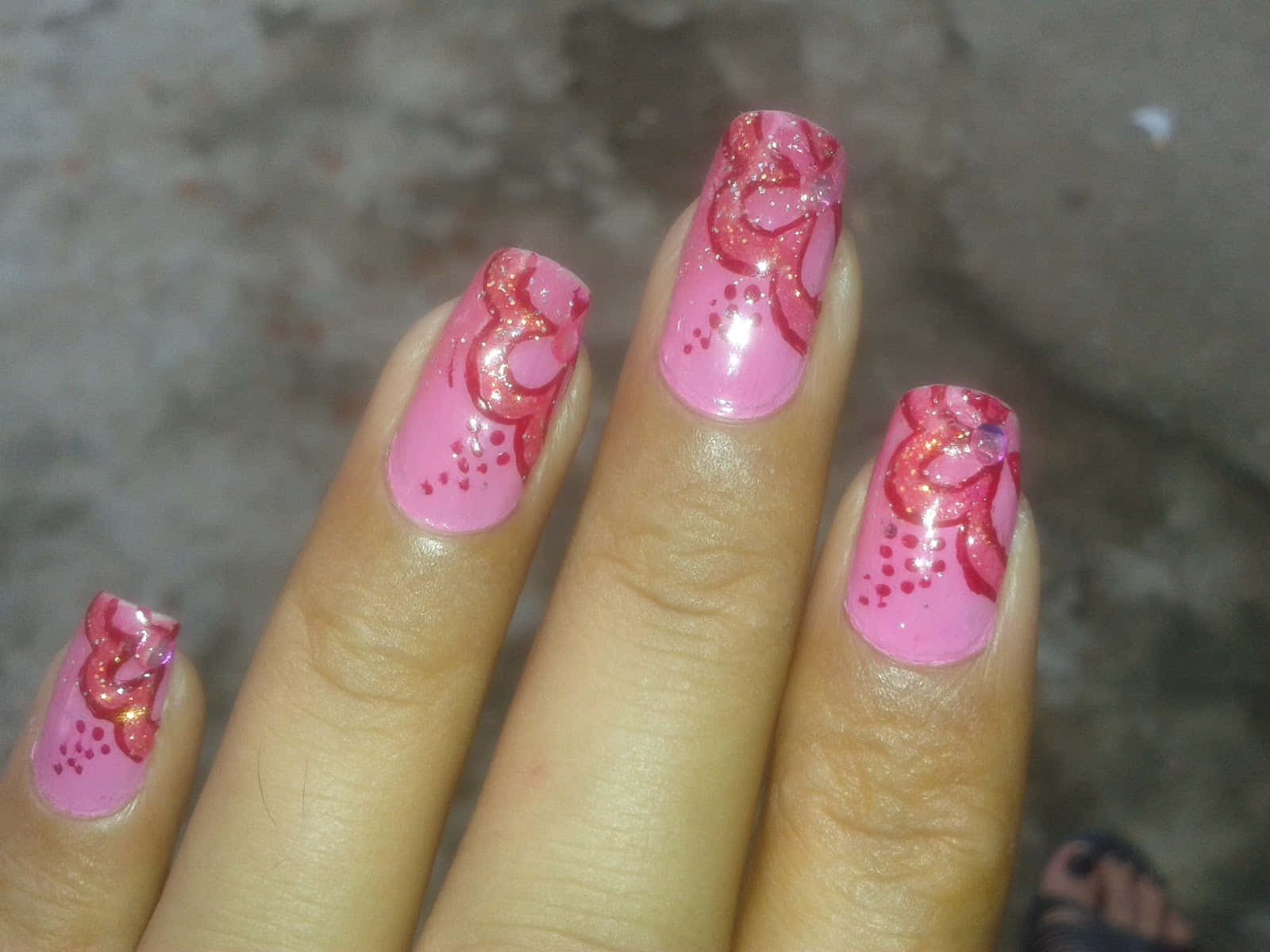 Pink Nails 桌布 壁紙 — 一隻手的特寫，粉紅色閃粉指甲上有紅色漩渦和圓點，背景是模糊的混凝土。