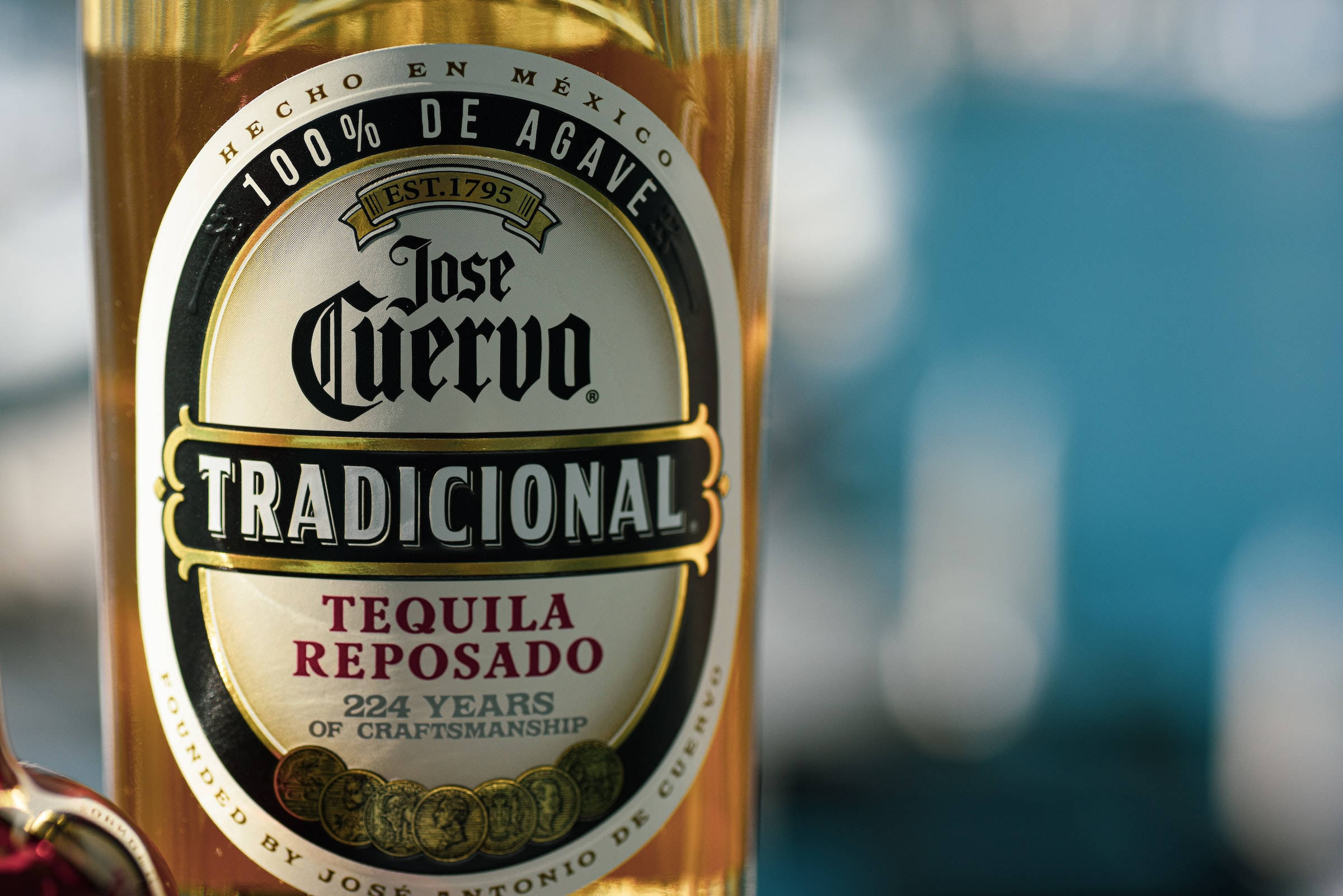 alcohol 桌布 壁紙 — Jose Cuervo Tradicional Tequila Reposado 酒瓶特寫，金色液體和詳細標籤，背景模糊藍色。