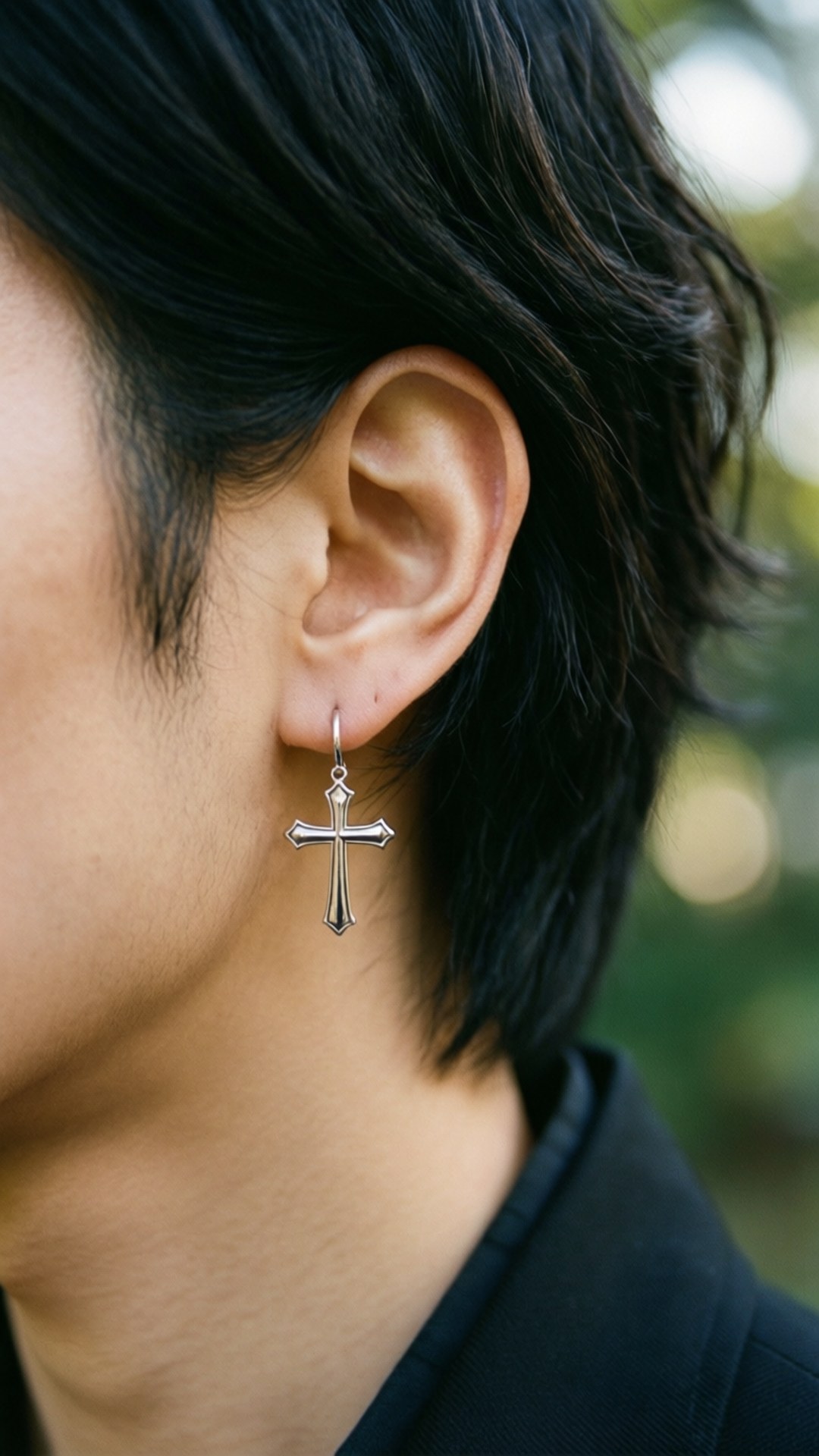 Cross Earring Detail 壁紙 — 特寫一個人戴著銀色十字架耳環的耳朵，背景是深色頭髮和模糊的綠色背景。