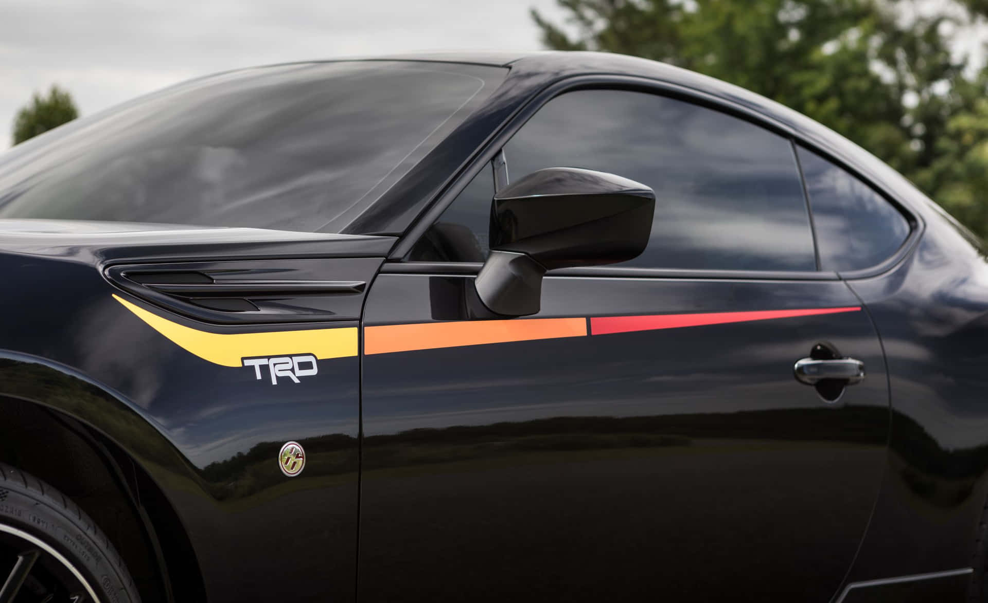 黑色跑車，側門上有色彩繽紛的 TRD 賽車條紋。 — Toyota Supra 壁紙