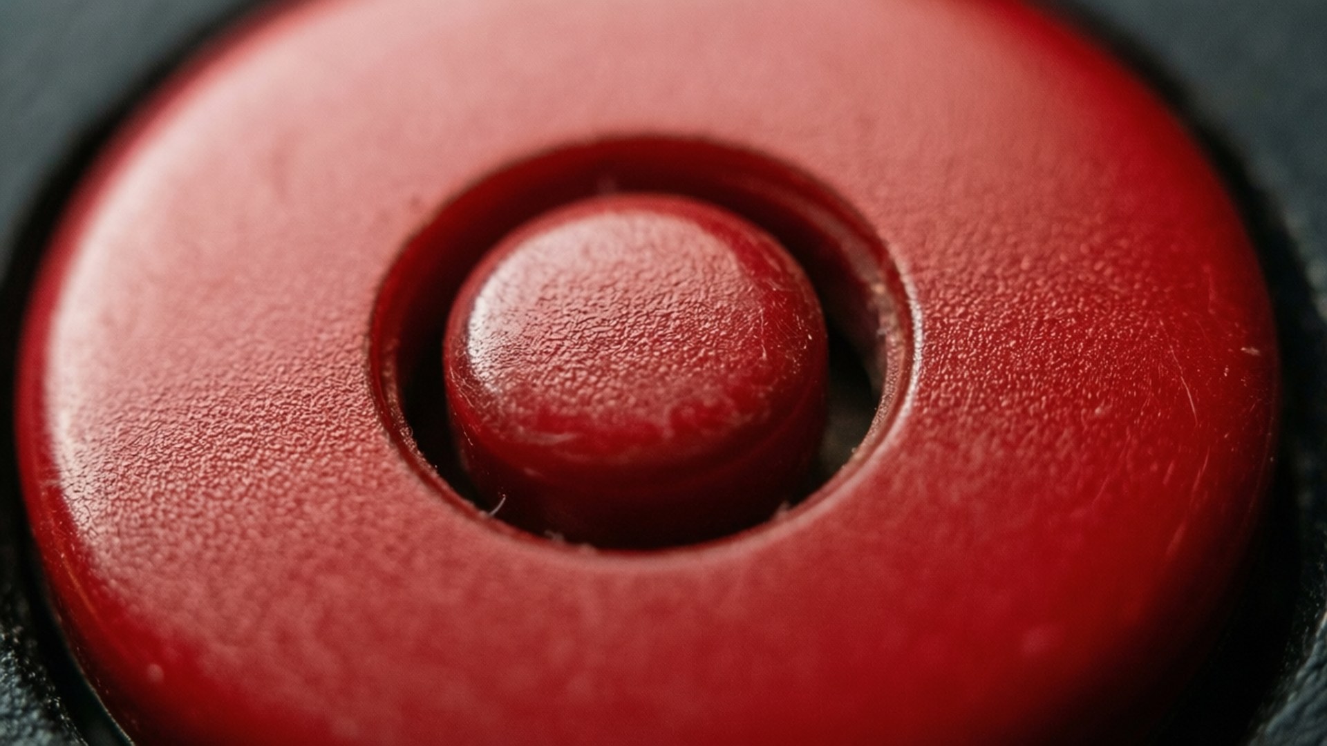 Red Circle Button Macro 壁紙 — 一個帶有中央突起的紋理紅色按鈕的特寫，背景為深色。
