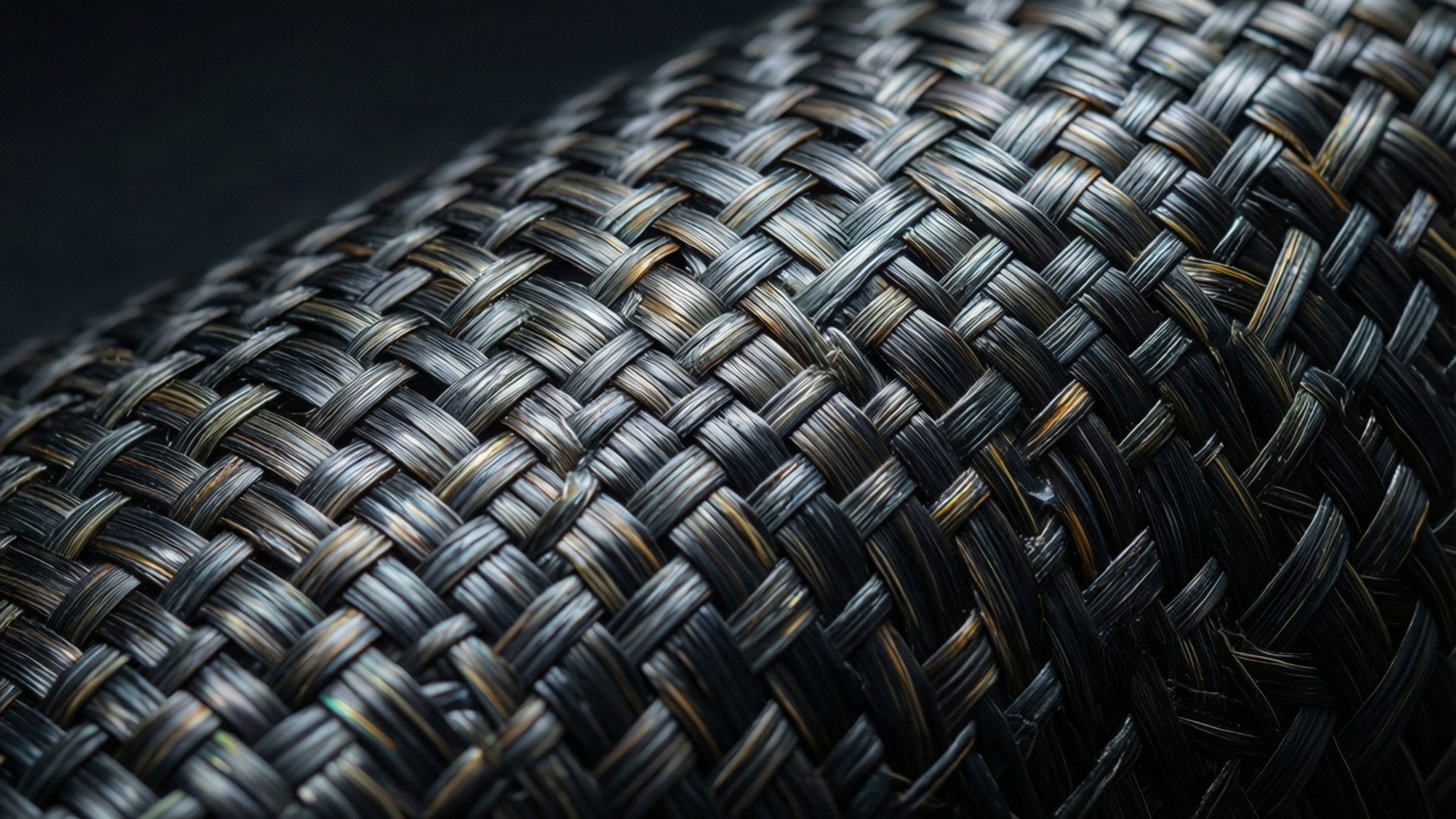 Woven Carbon Fiber Macro 壁紙 — 柔軟燈光下，緊密編織的深灰色和黑色紋理布料的特寫，帶有微妙的金色亮點。