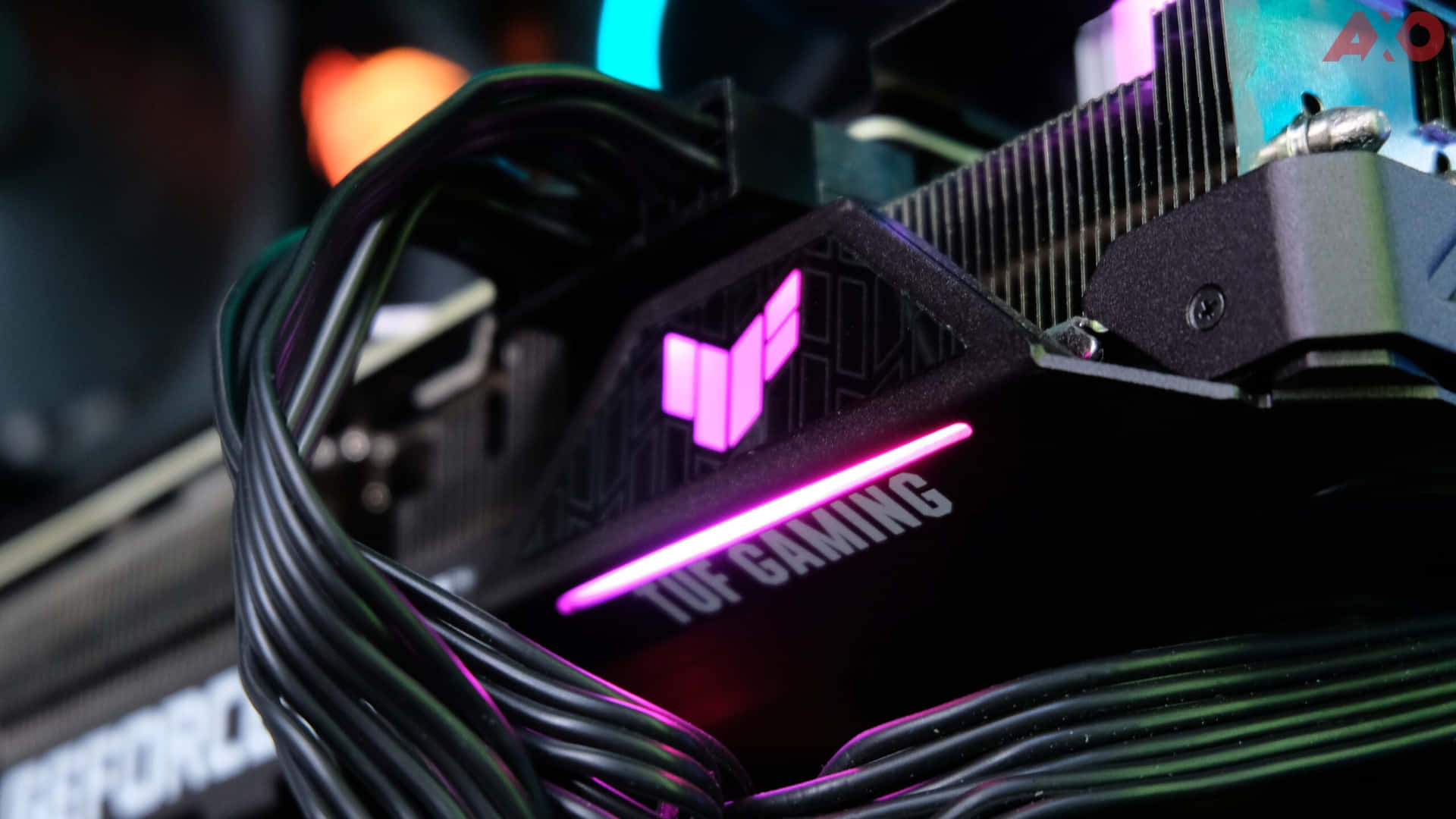  壁紙 — TUF Gaming 顯示卡特寫，帶有發光的粉紅色 LED 裝飾和黑色電纜，處於黑暗的科技設置中。