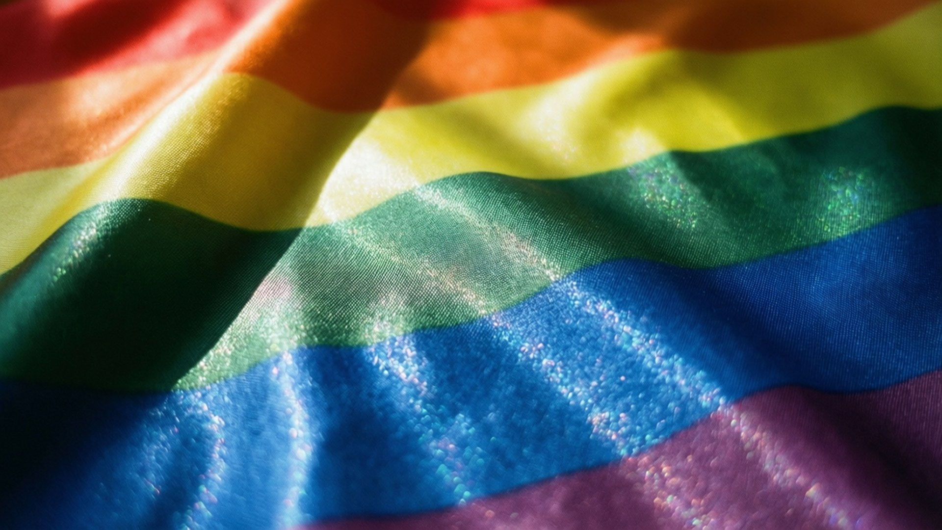 Shimmering Pride Fabric 壁紙 — 充滿活力的彩虹旗布料特寫，帶有光澤的褶皺，捕捉光線，呈現鮮豔的紅、橙、黃、綠、藍和紫色條紋。