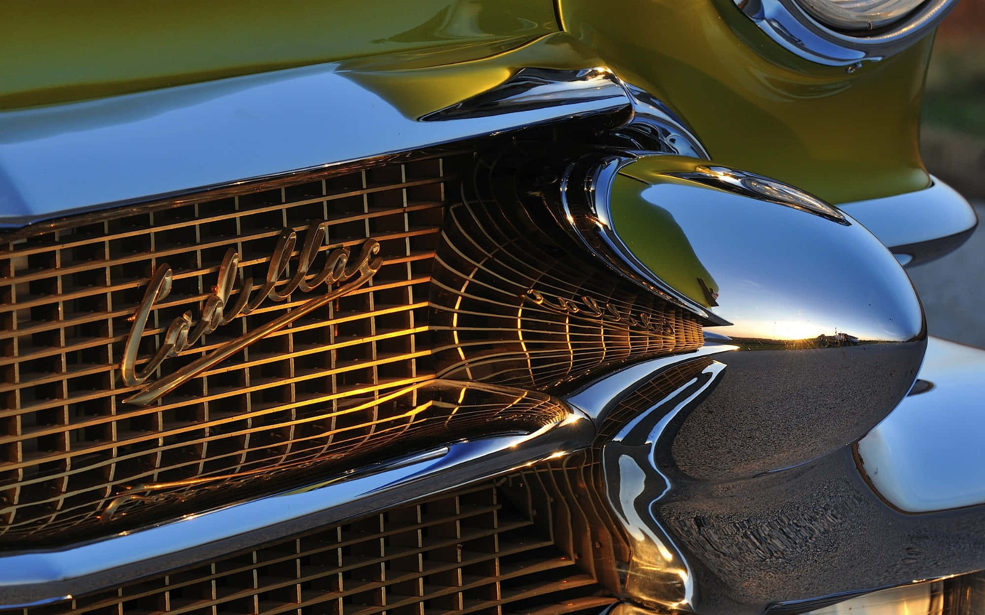 Cadillac Deville 桌布 壁紙 — 經典凱迪拉克閃亮鍍鉻格柵和引擎蓋飾物特寫，反射金色夕陽光芒。