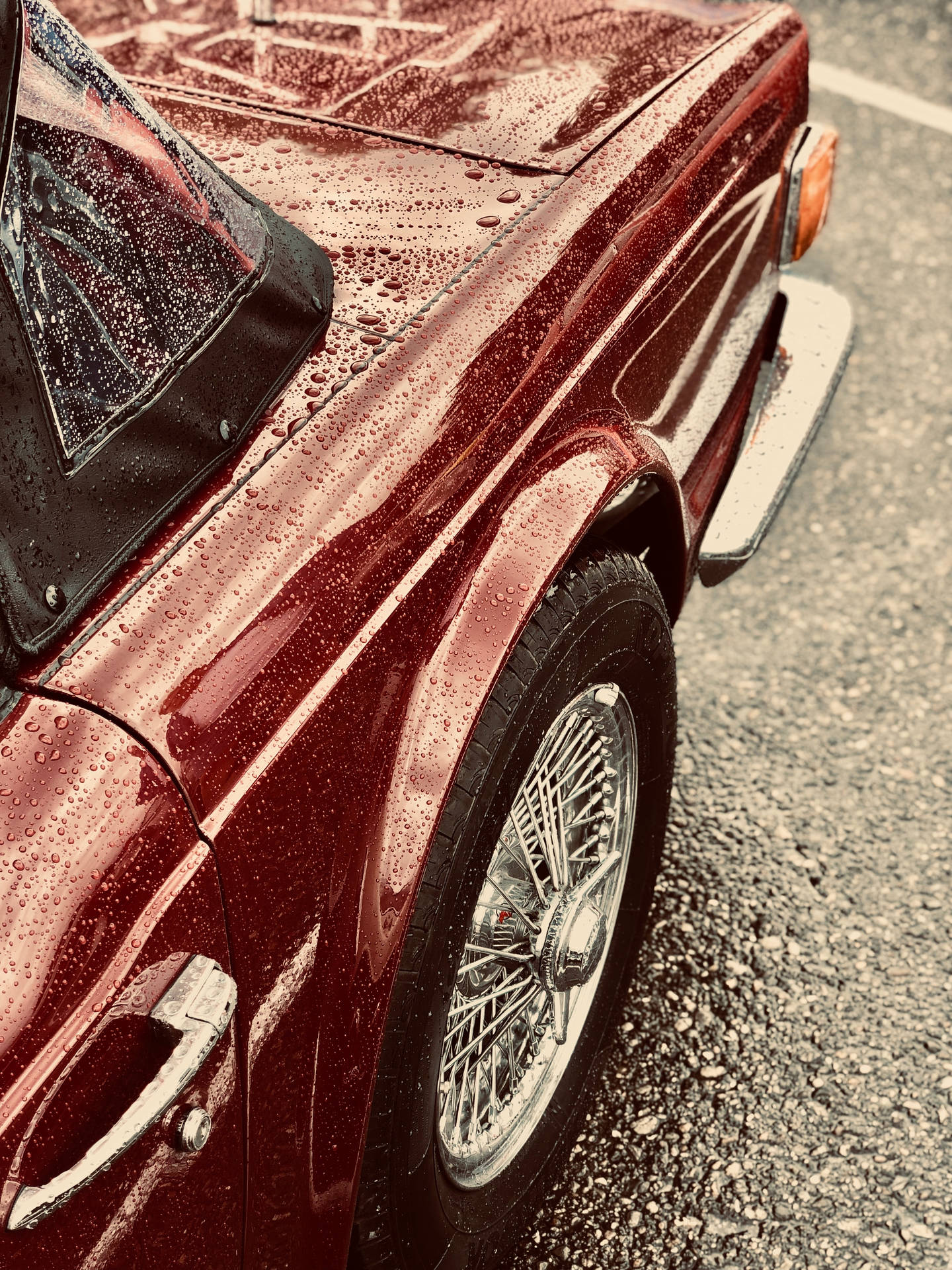復古紅色敞篷車的特寫，引擎蓋和鋼絲輪圈上有雨滴。 — Chromebook 壁紙