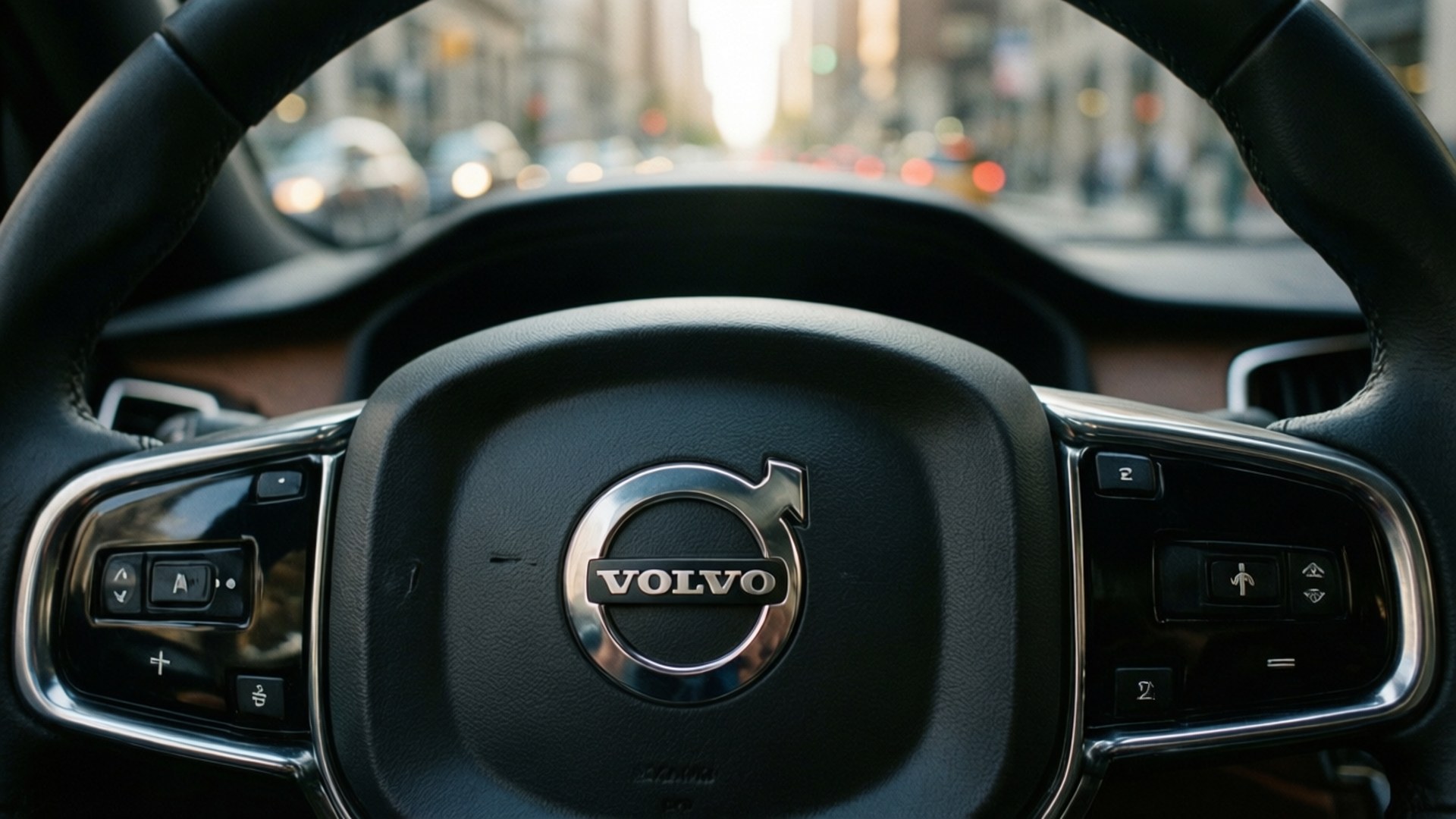 Volvo Logo Close-Up 壁紙 — 沃爾沃汽車方向盤特寫，帶有鍍鉻裝飾和控制按鈕，背景是模糊的城市街道。