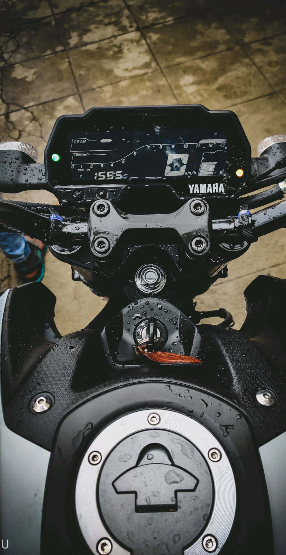  壁紙 — 濕掉的Yamaha機車儀表板和油箱特寫，雨滴在黑色金屬和混凝土地面上閃閃發光。