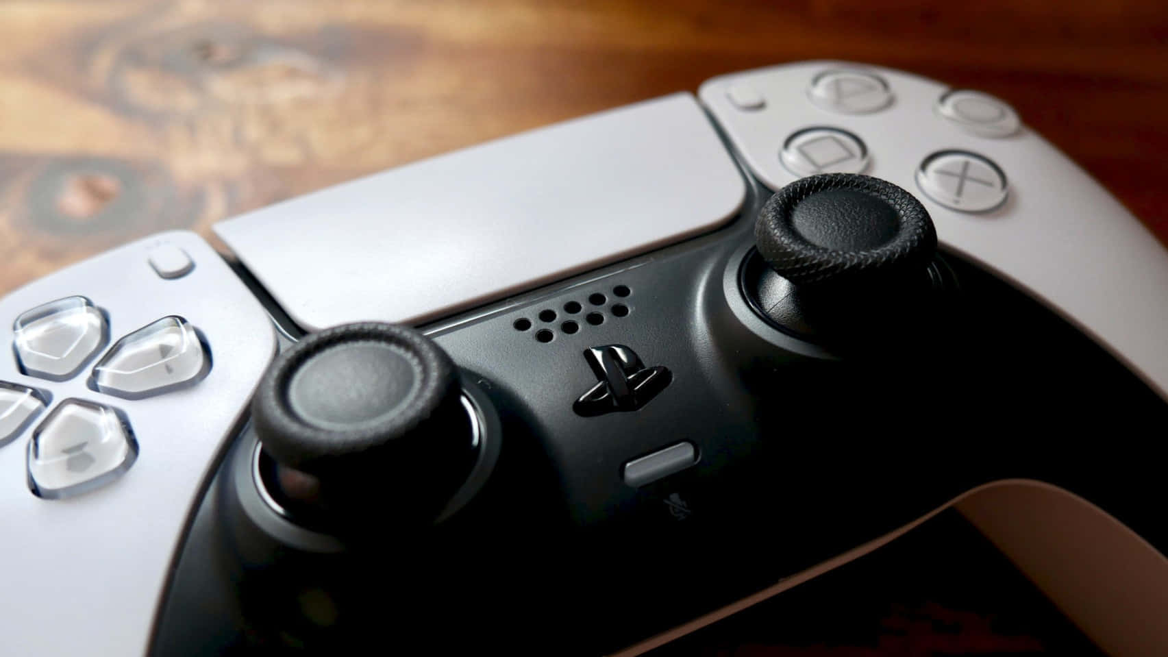  壁紙 — 白色和黑色PlayStation 5手把的特寫，放置在木質表面上，帶有溫暖的燈光。
