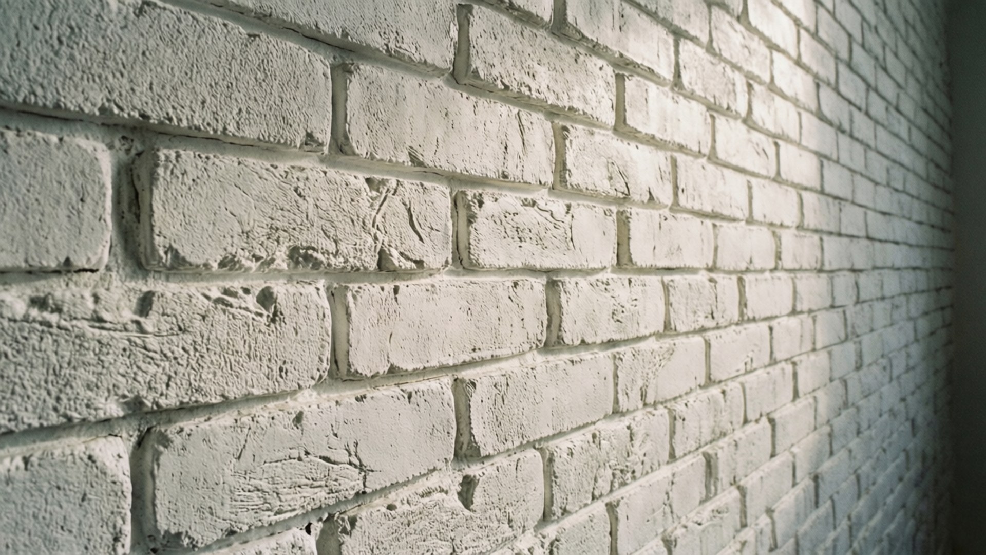 Embossed Faux White Brick 壁紙 — 白色磚牆的特寫，帶有紋理灰泥線條和柔和的方向性照明。