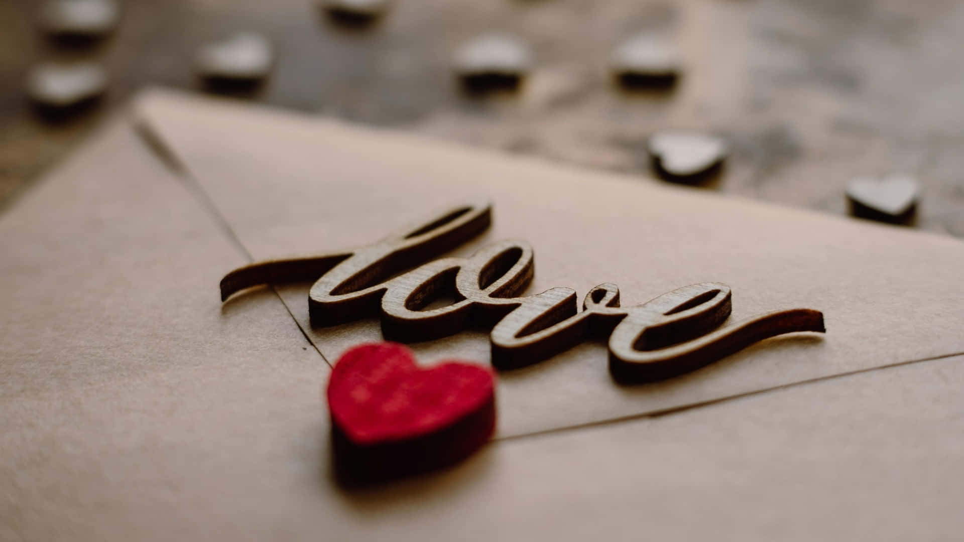  壁紙 — 一個木製的「love」標誌和紅色心形在棕色信封上的特寫，背景有模糊的心形鈕扣。