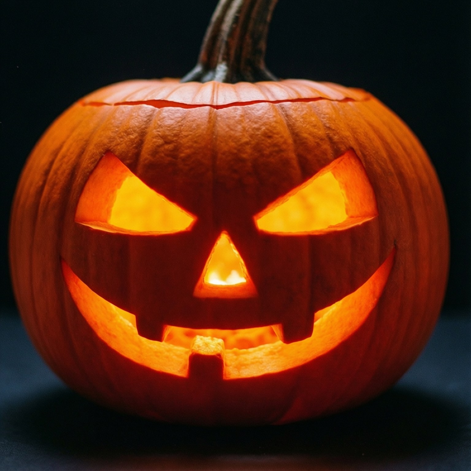 Neon Orange Halloween Pumpkin 壁紙 — 一個雕刻的橙色南瓜特寫，在黑暗背景上帶有發光的眼睛、鼻子和鋸齒狀的笑容。
