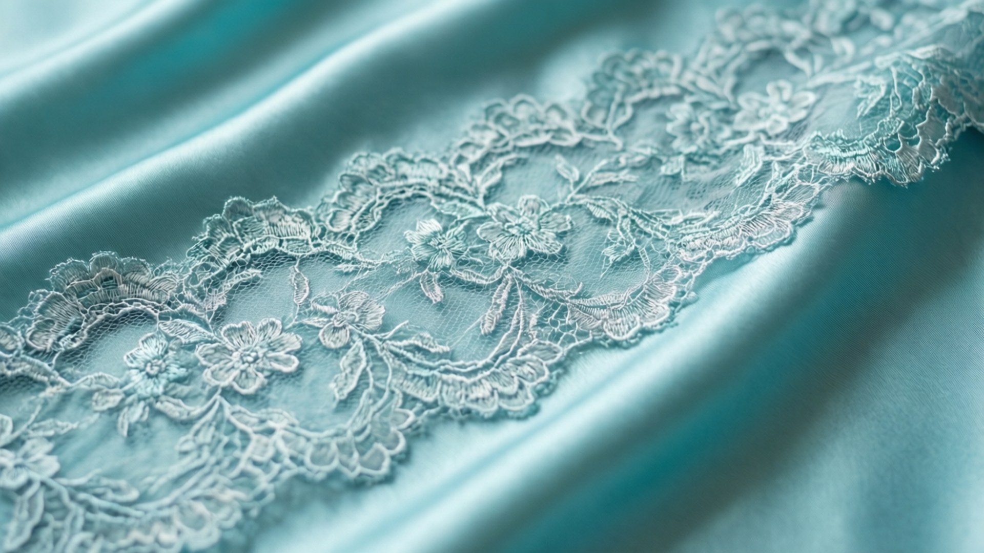 Chantilly-tiffany 桌布 壁紙 — 精緻白色花卉蕾絲飾邊縫在光滑的藍綠色緞面布料上，帶有柔軟褶皺的特寫。