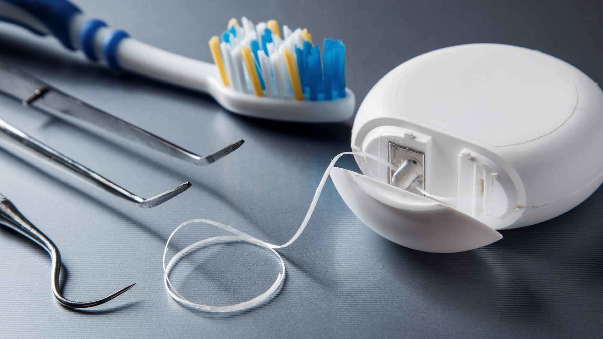  壁紙 — 牙科工具的特寫，包括牙刷、牙線容器和金屬器械，排列在灰色表面上。