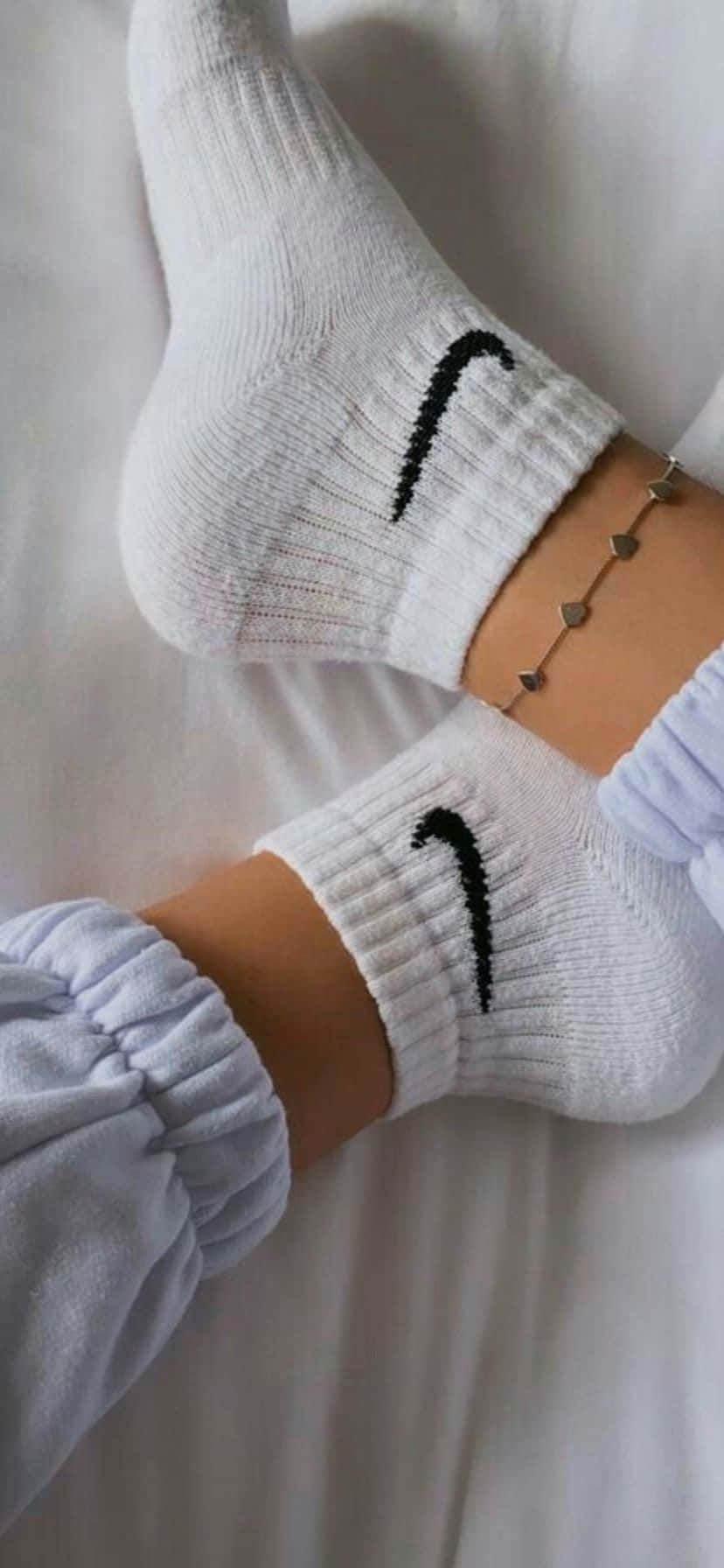  壁紙 — 穿著白色Nike襪子的腳部特寫，腳上戴著精緻的銀色腳鍊，擱在柔軟的白色床上。