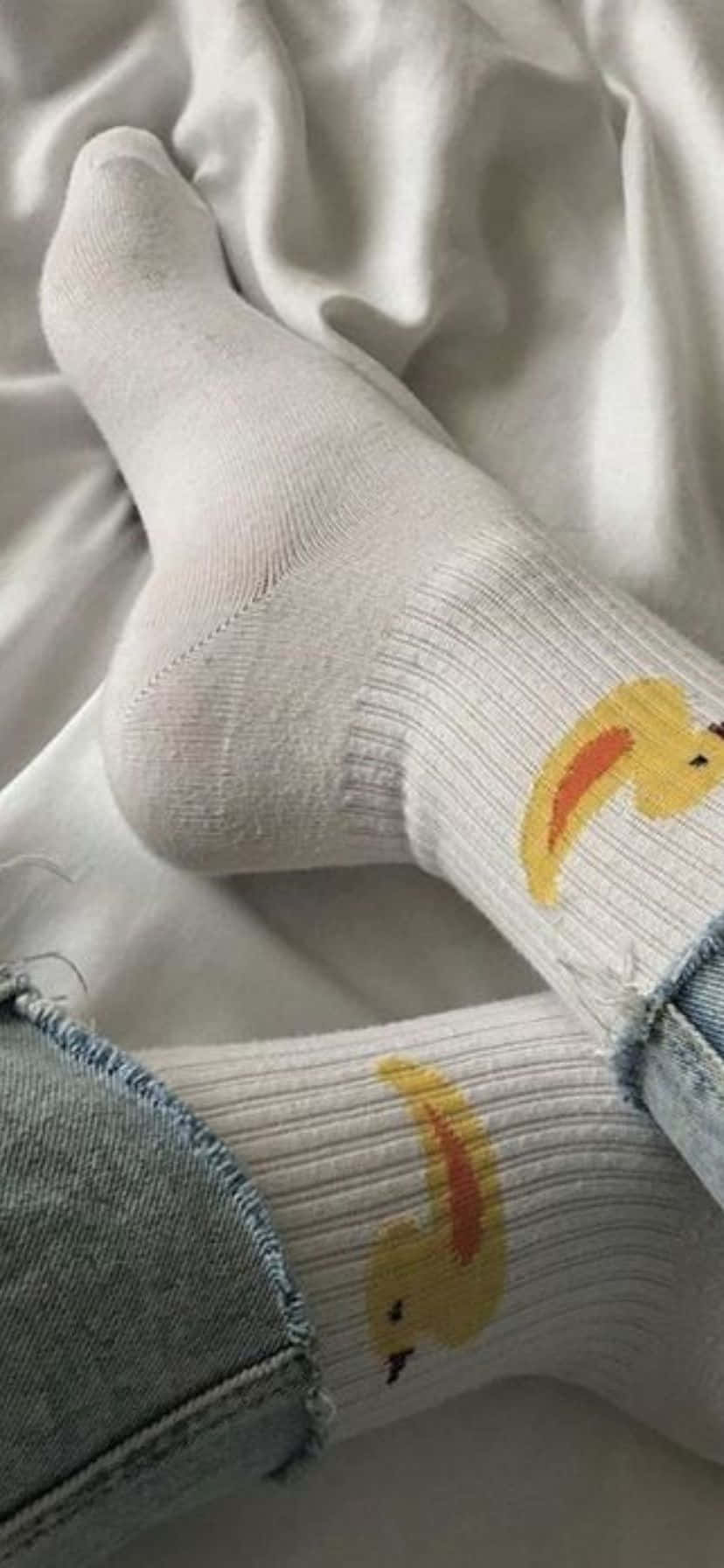  壁紙 — 一雙穿著帶有黃色鴨子圖案白色襪子的腳，擱在柔軟的白色布料上，特寫鏡頭。
