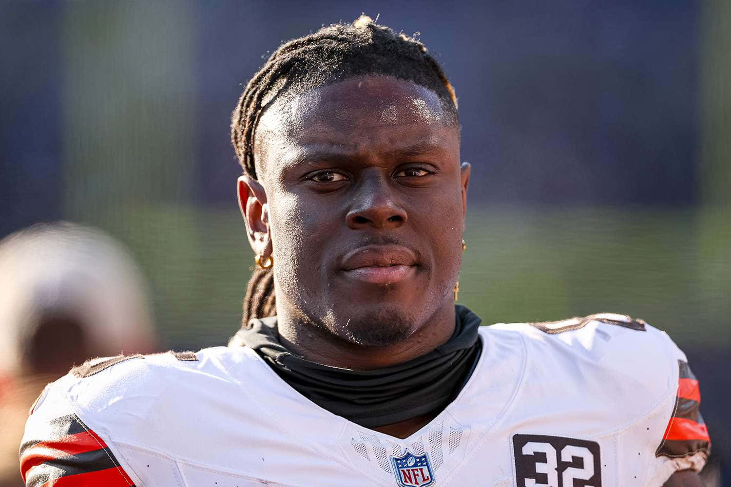 壁紙 — 一位專注的NFL美式足球員在陽光明媚的球場上，身穿白色球衣，號碼32，帶有棕橙色點綴的特寫。