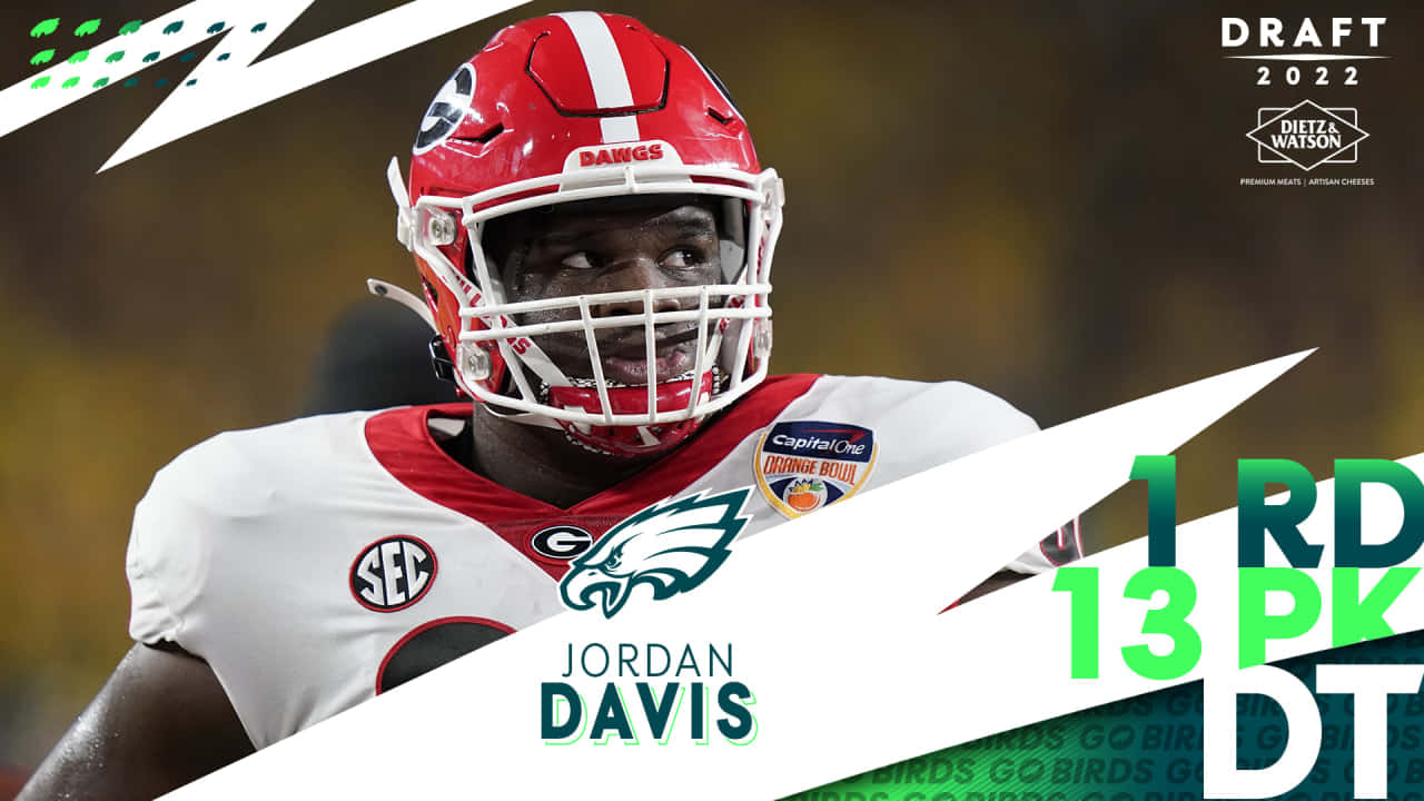  壁紙 — 美式足球員 Jordan Davis 的近距離特寫，戴紅色頭盔，身穿印有 'BIRDS' 標誌的白色球衣，背景是模糊的球場及選秀資訊圖表。