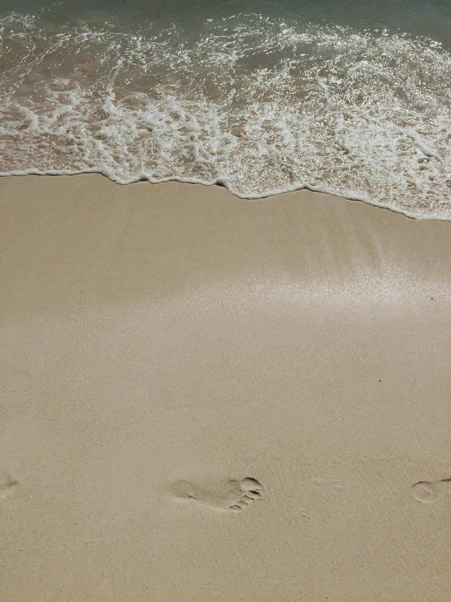  壁紙 — 一個特寫鏡頭，溫柔的海浪沖刷著光滑的棕褐色沙灘，水邊附近有一個清晰的腳印。