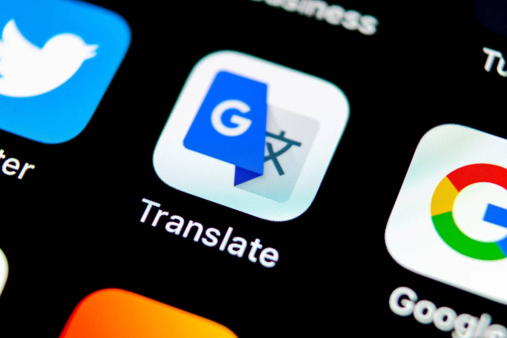 Google Translate 桌布 壁紙 — Google Translate 應用程式圖標在黑暗的智慧型手機螢幕上發光的特寫，附近有其他應用程式圖標。