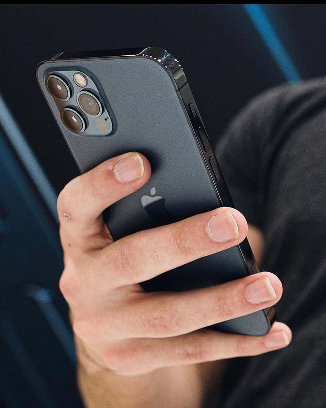 手拿著帶有三鏡頭的深灰色iPhone 12 Pro。 — iPhone 13 Pro Max 壁紙