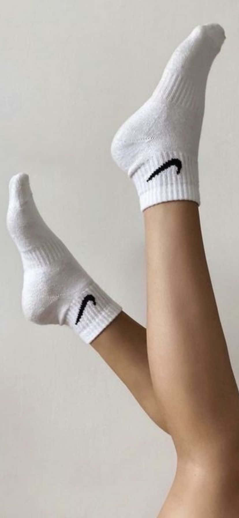  壁紙 — 雙腿穿著帶有黑色 swoosh 的白色 Nike 襪子，靠著素色牆壁的特寫。