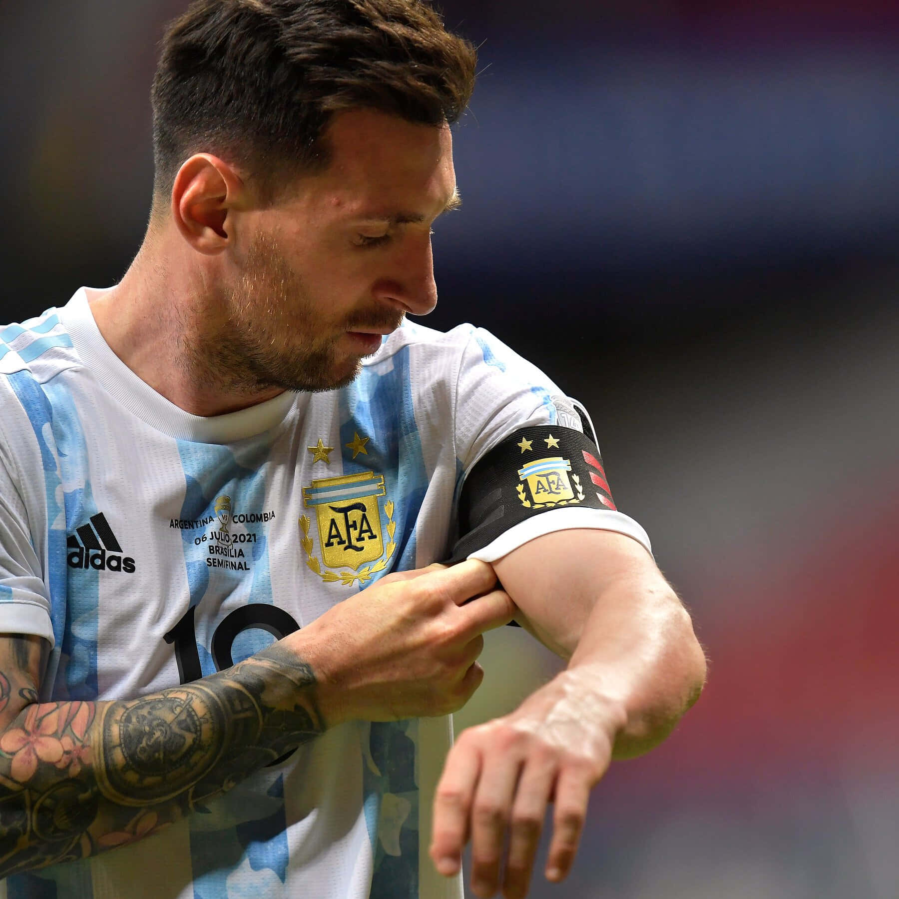 Messi 2022 桌布 壁紙 — 里奧內爾·梅西在阿根廷足球比賽中調整隊長臂章的近距離特寫，身穿藍白條紋球衣。