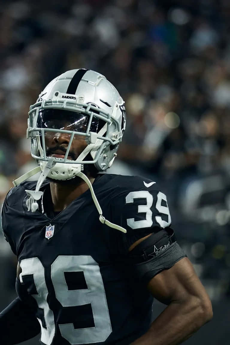  壁紙 — NFL 美式足球員的近距離特寫，身穿黑色和銀色的 Raiders 球衣，號碼 39，在球場燈光下比賽期間站在場上。