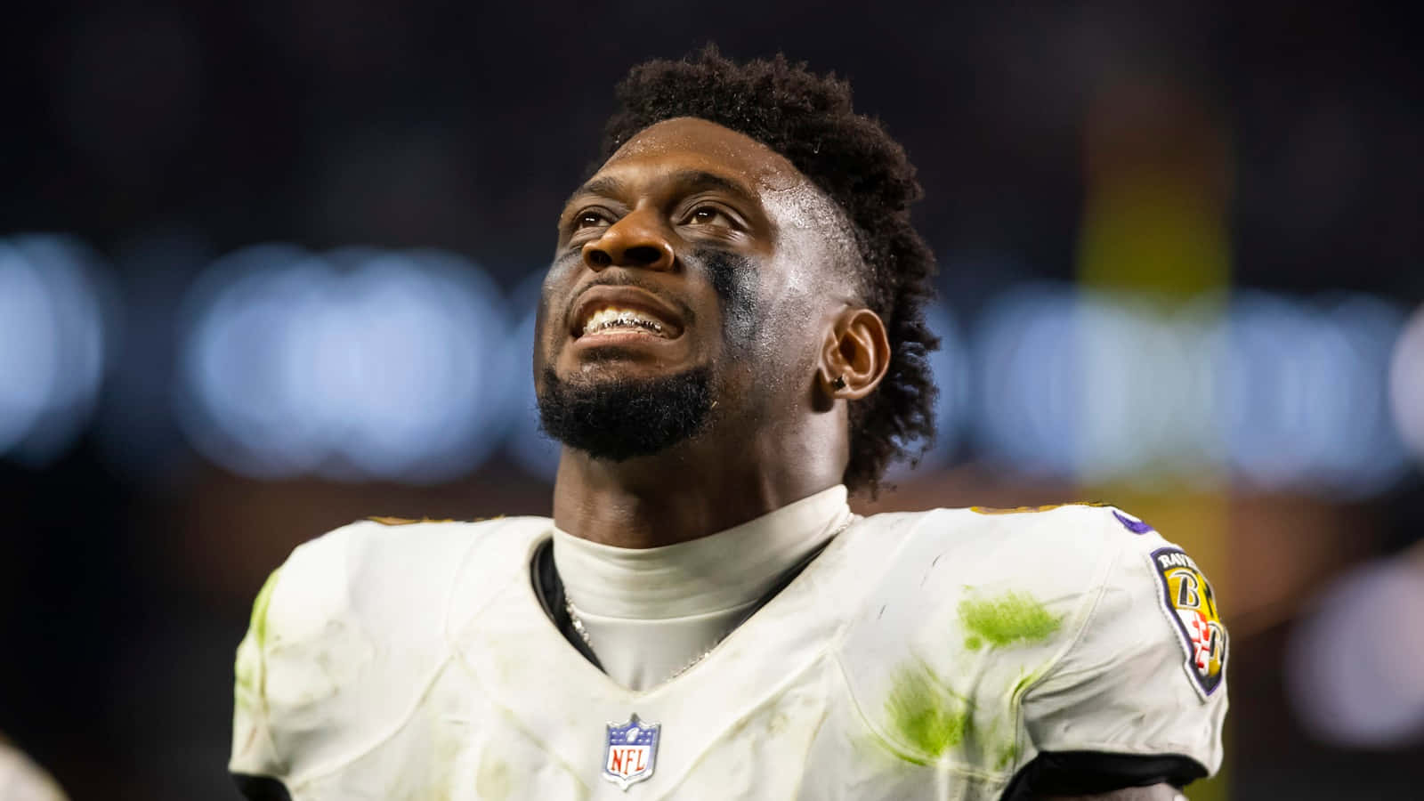  壁紙 — NFL 美式足球員臉部和球衣沾有污垢，夜晚在球場向上看的特寫。