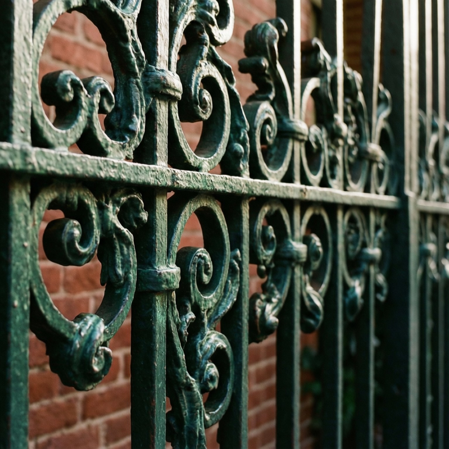 Wrought Iron Scrollwork Detail 壁紙 — 紅色磚牆前華麗綠色鍛鐵圍欄帶漩渦圖案的近距離特寫。
