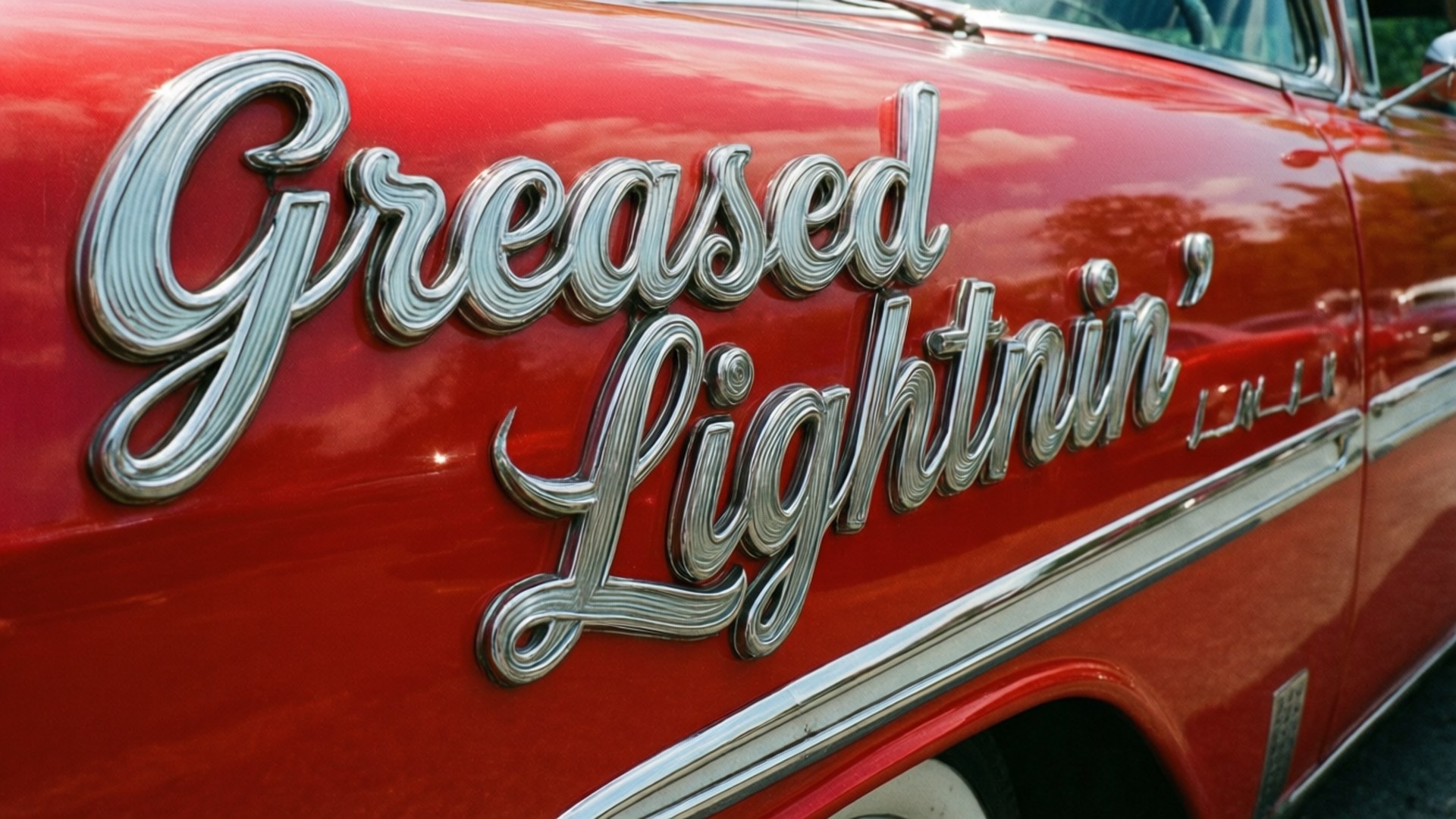 油脂 桌布 壁紙 — 閃亮鍍鉻 'Greased Lightnin'' 字體在光澤紅色經典車門上的特寫。