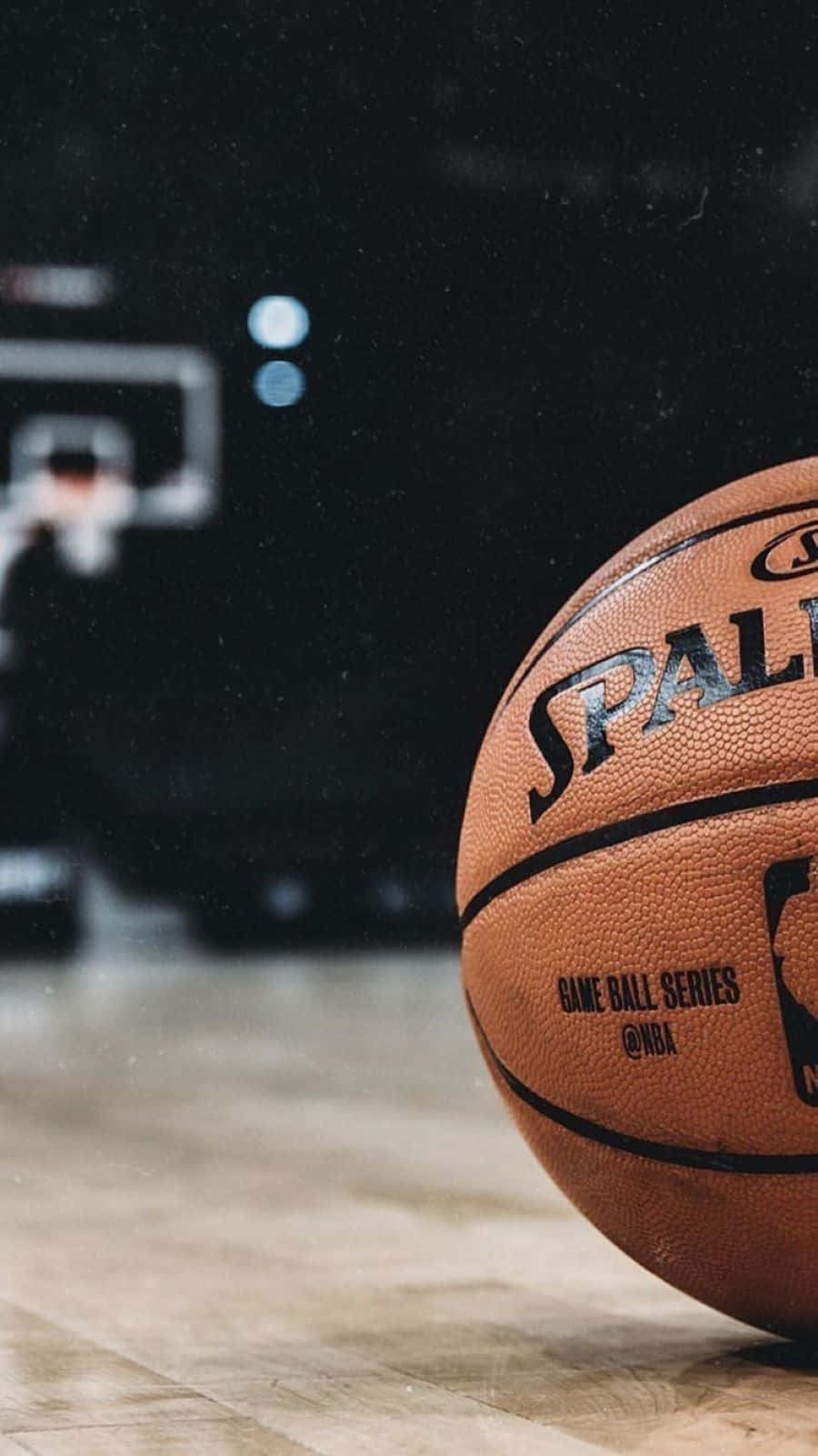 壁紙 — 一個Spalding NBA比賽用球的特寫，放置在拋光木地板上，背景有模糊的籃框。