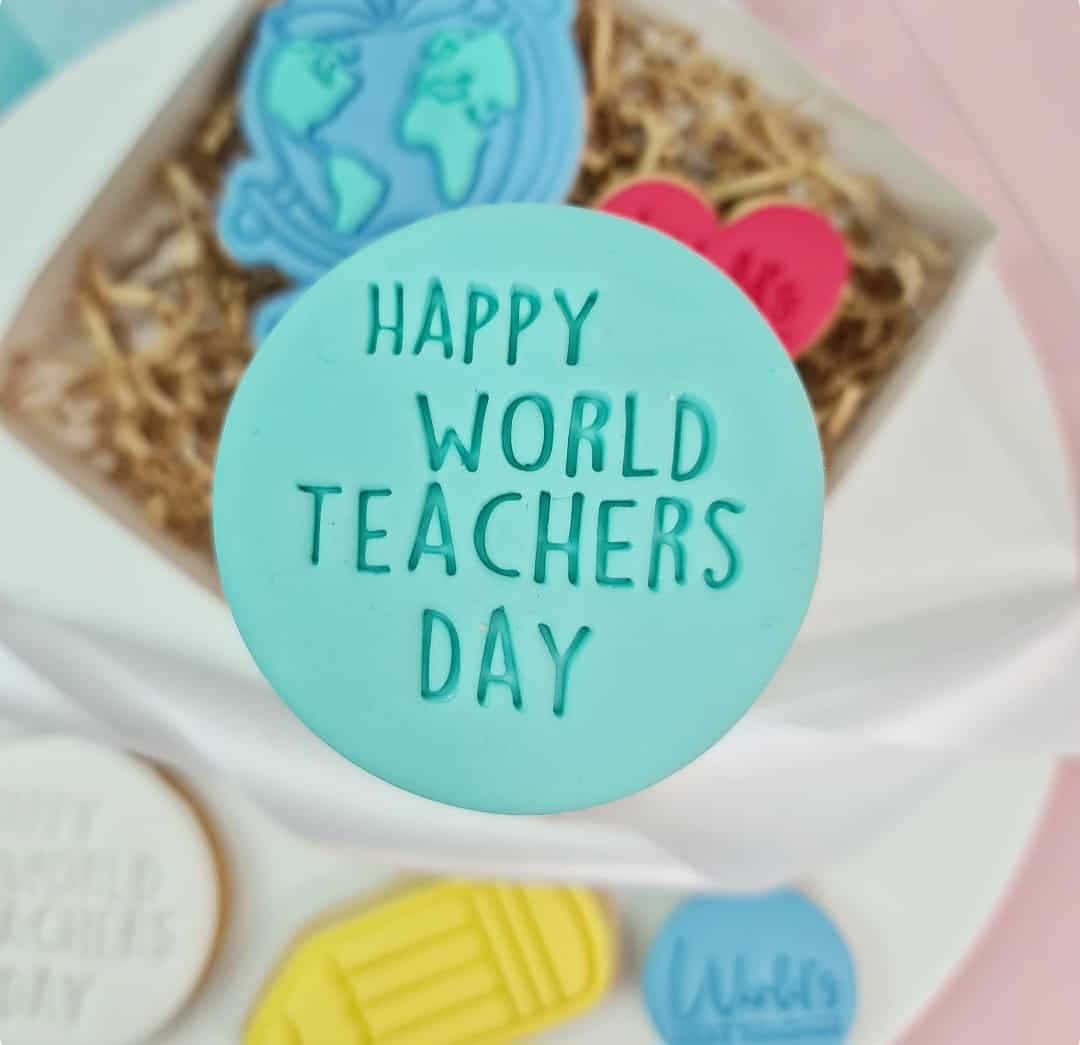 壁紙 — 一個青綠色圓形餅乾的特寫，上面有浮雕文字「HAPPY WORLD TEACHERS DAY」，周圍環繞著其他主題餅乾和一個禮物盒。