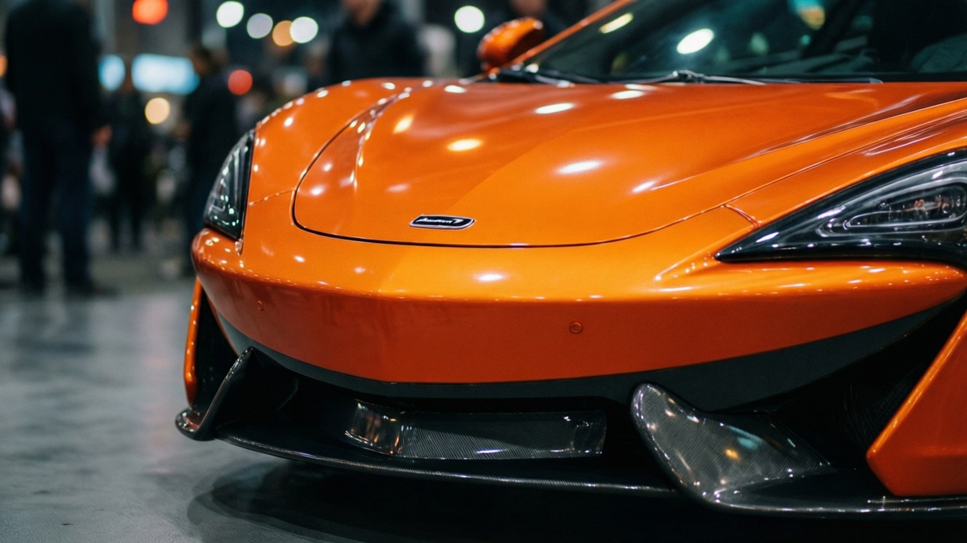 Mclaren 570gt 桌布 壁紙 — 室內車展中，一輛鮮橙色McLaren跑車在明亮燈光下閃閃發光的特寫。
