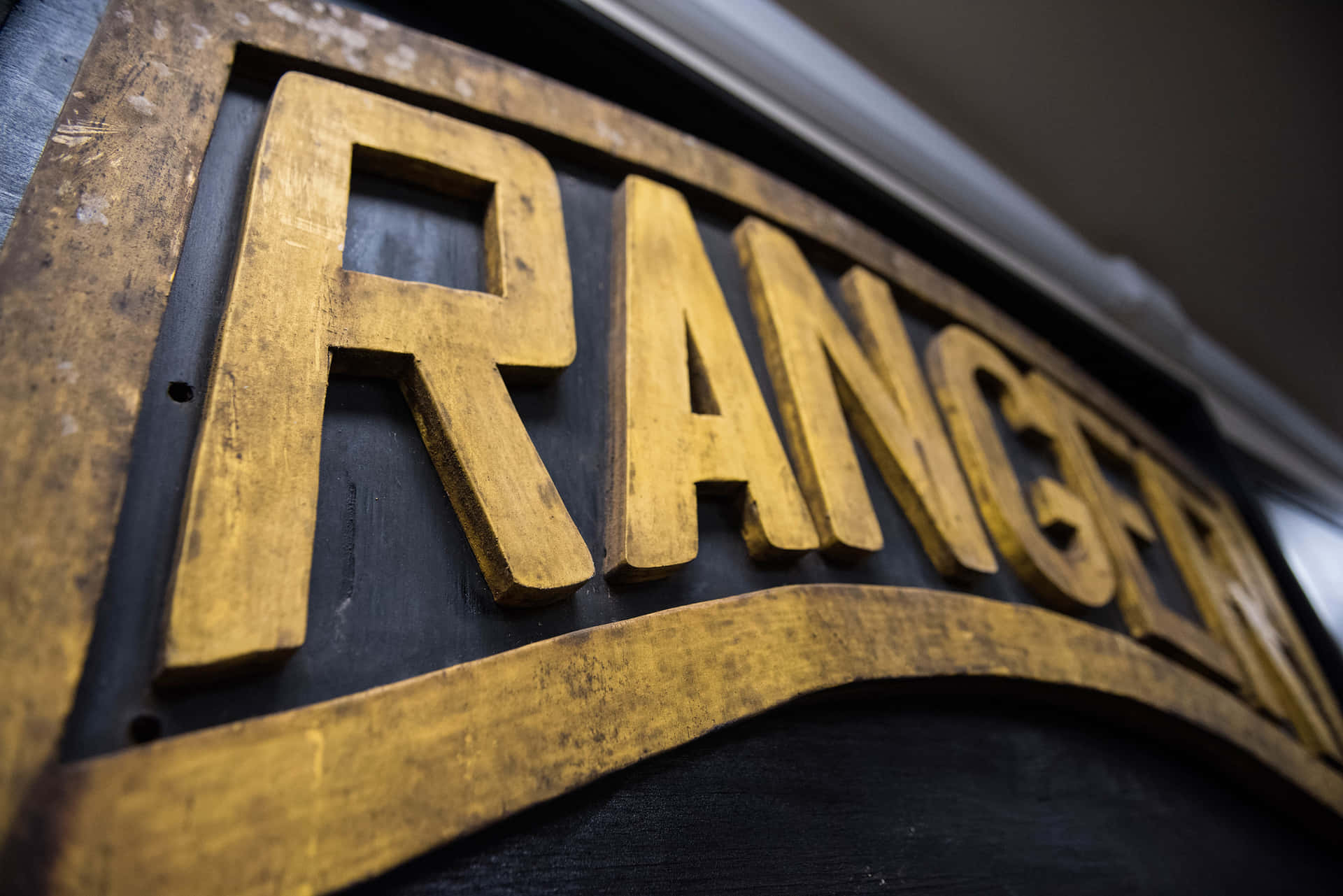  壁紙 — 特寫風化金色字母拼出 'RANGER' 在深色木牌上，可見紋理和深度。
