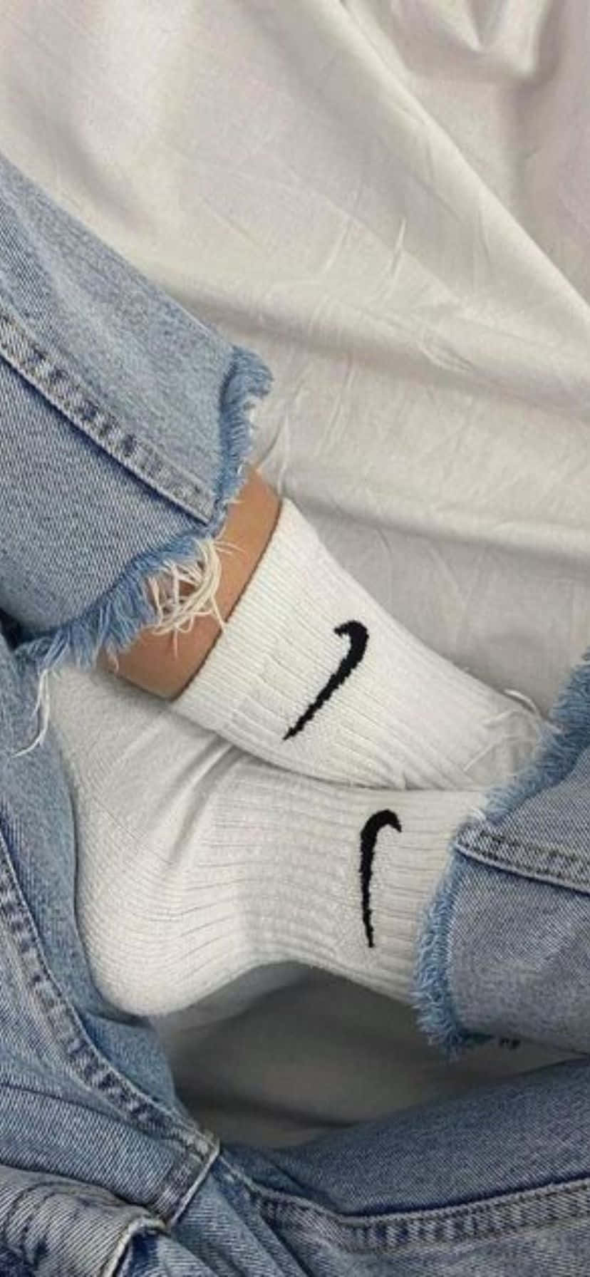  壁紙 — 白色Nike襪子從磨損的藍色牛仔褲中露出的特寫，背景為柔軟的白色布料。