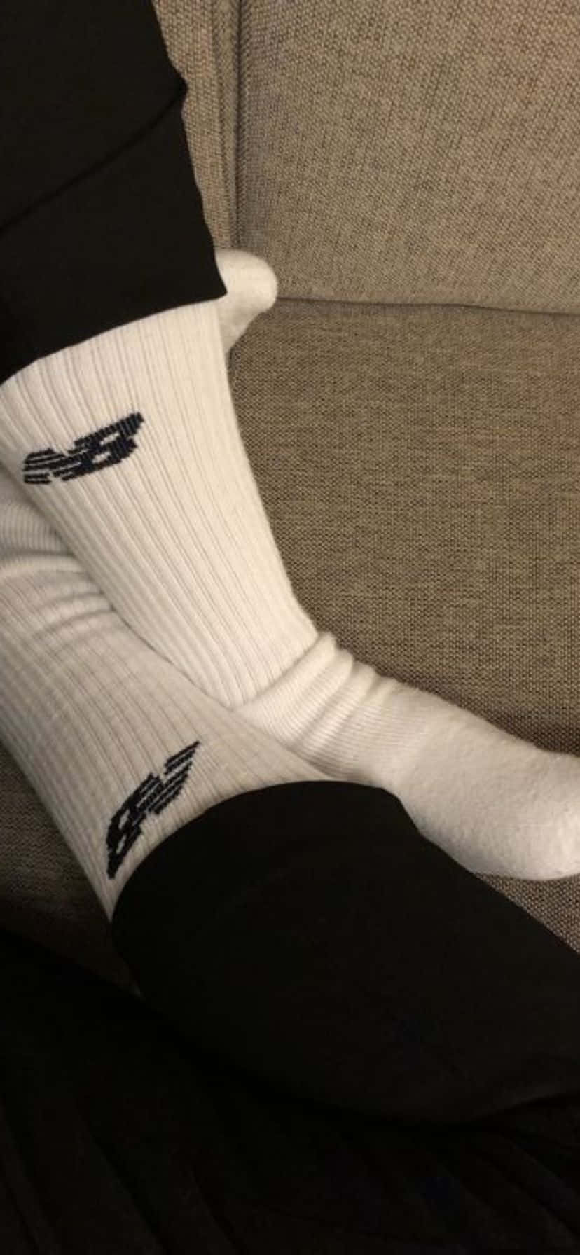  壁紙 — 米色紋理沙發上放著帶有黑色 New Balance 標誌的白色羅紋襪子的特寫。